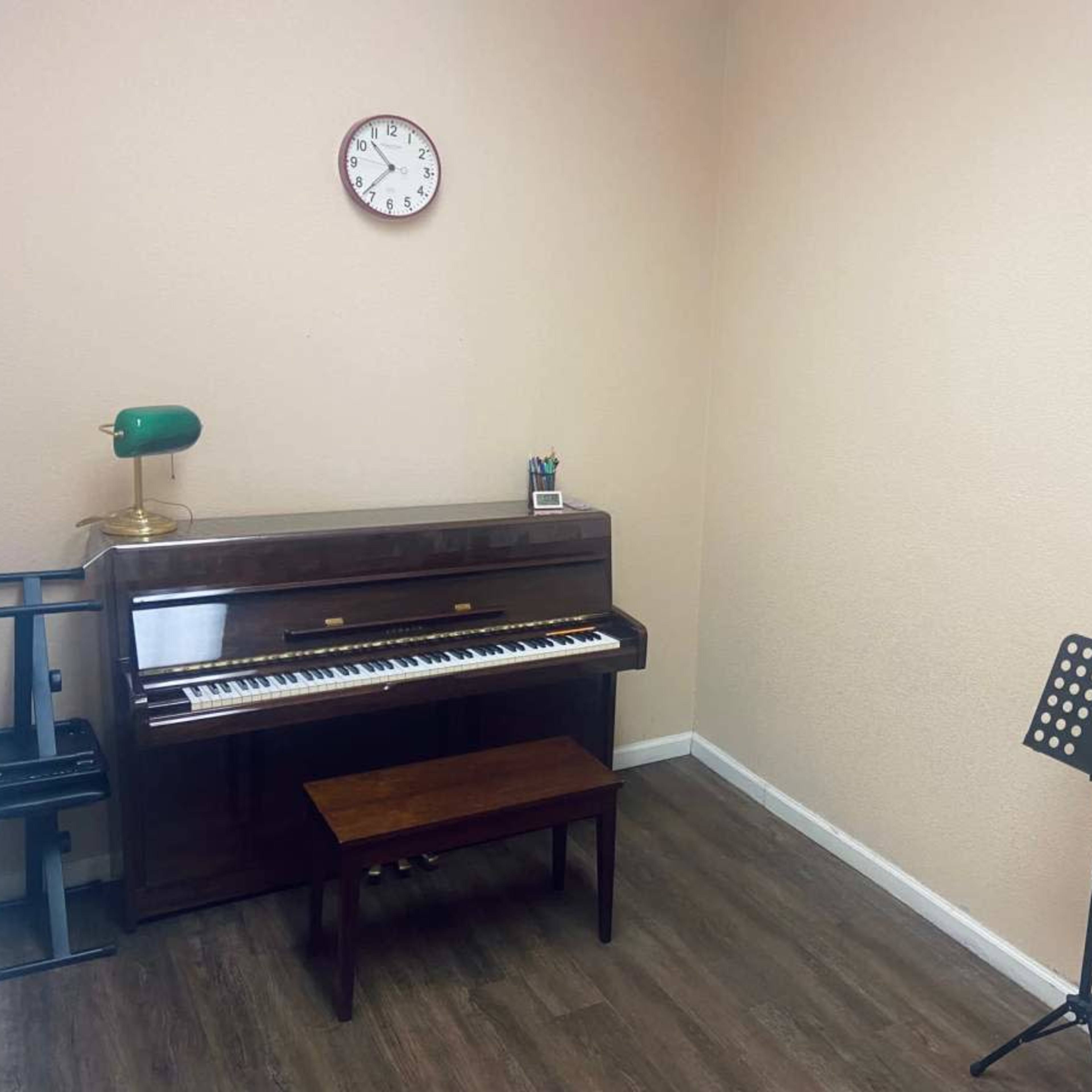 A small room with a wooden piano, a bench, a music stand, and a wall clock.