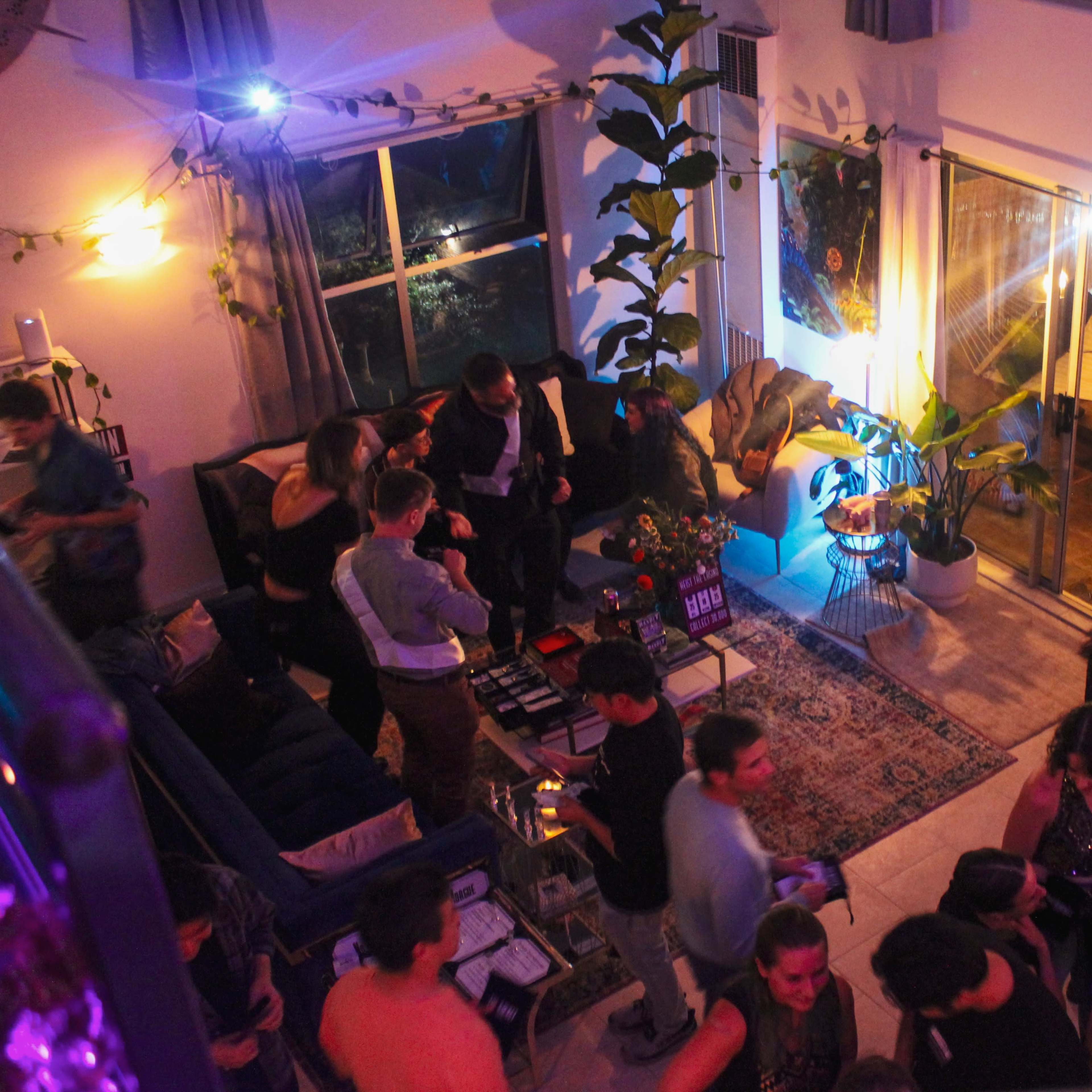 A group of people socializes in a brightly lit living room filled with plants and colorful decor.