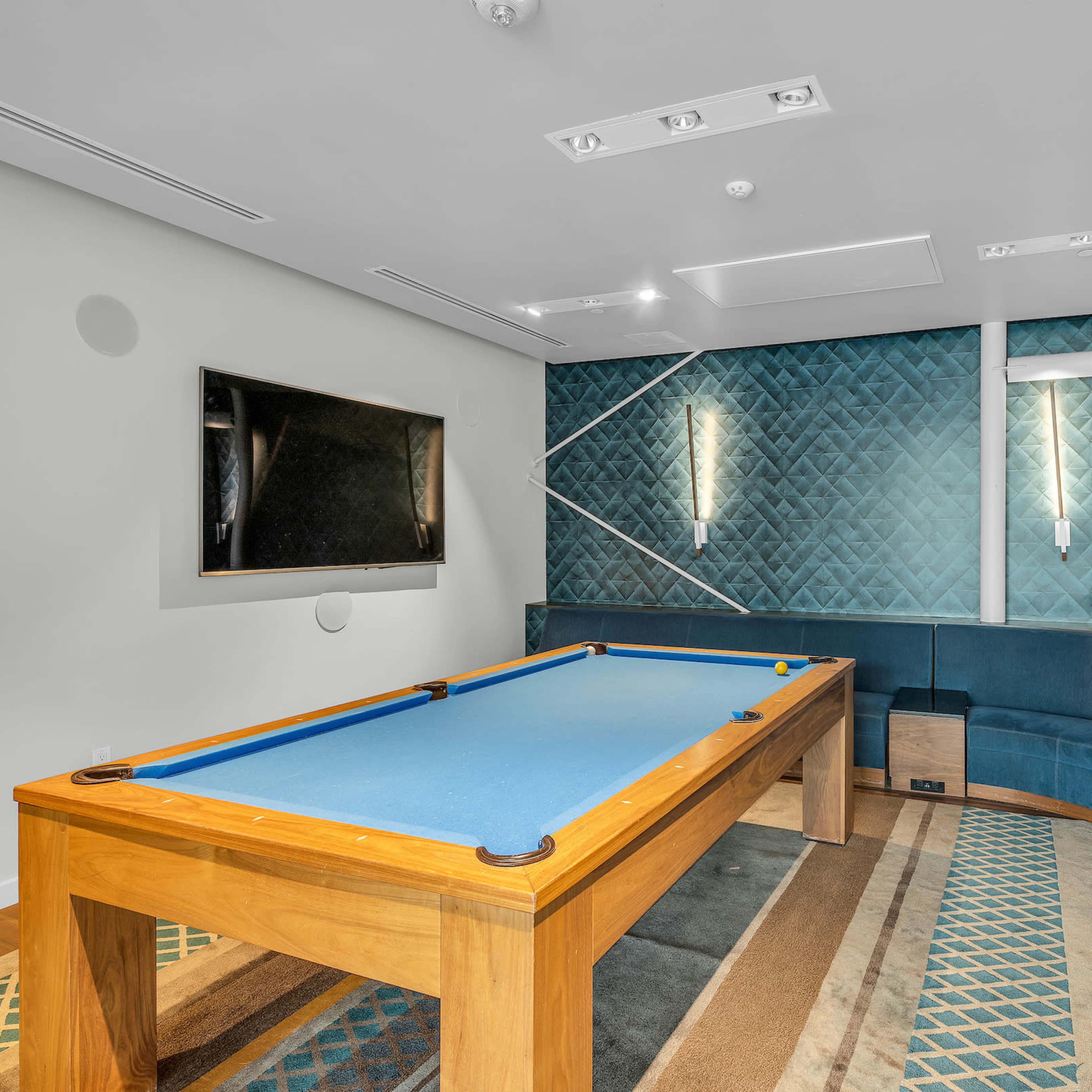A game room featuring a blue pool table, a curved seating area, and a wall-mounted television.
