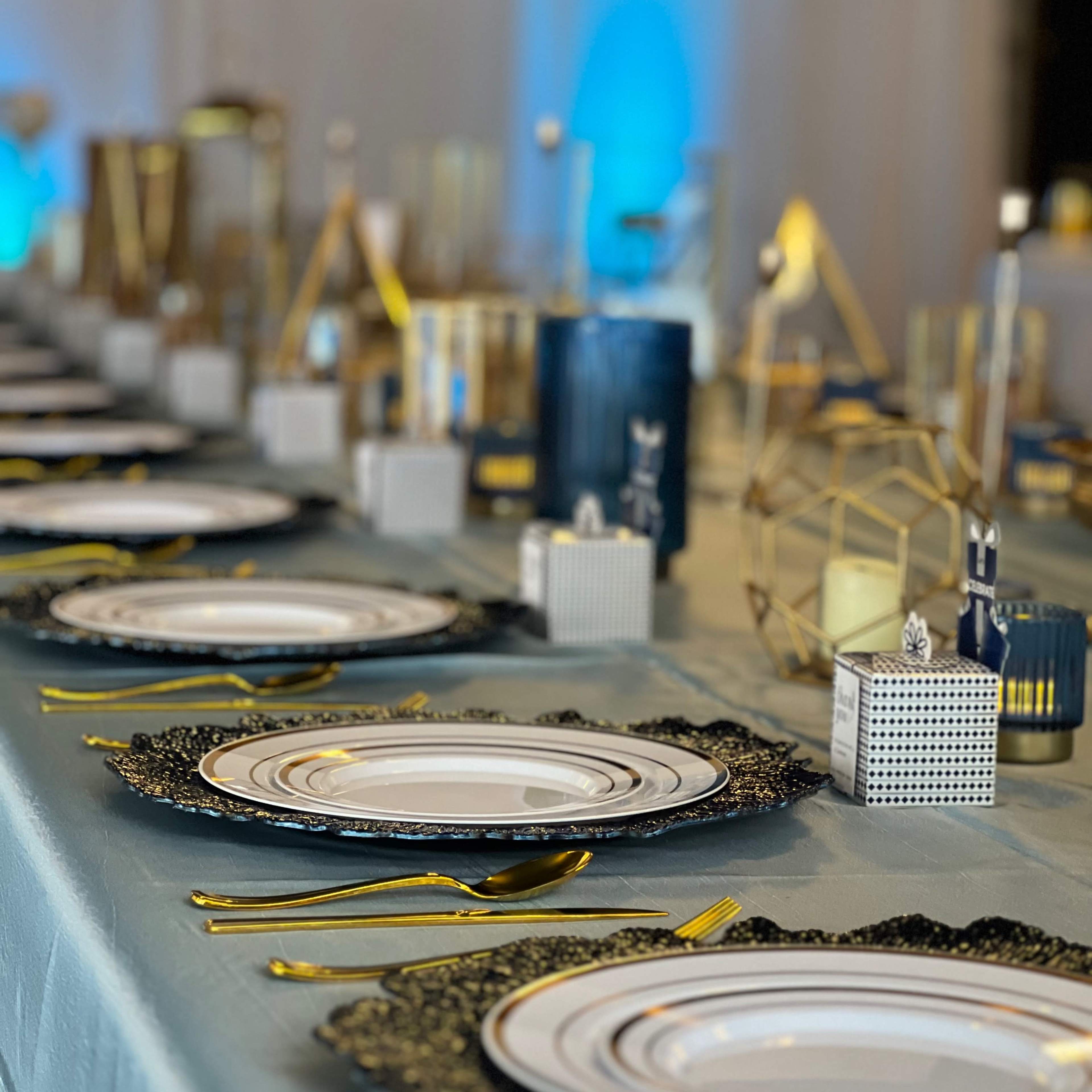 A long dining table is set with ornate plates and gold utensils, surrounded by decorative glassware and geometric centerpieces.