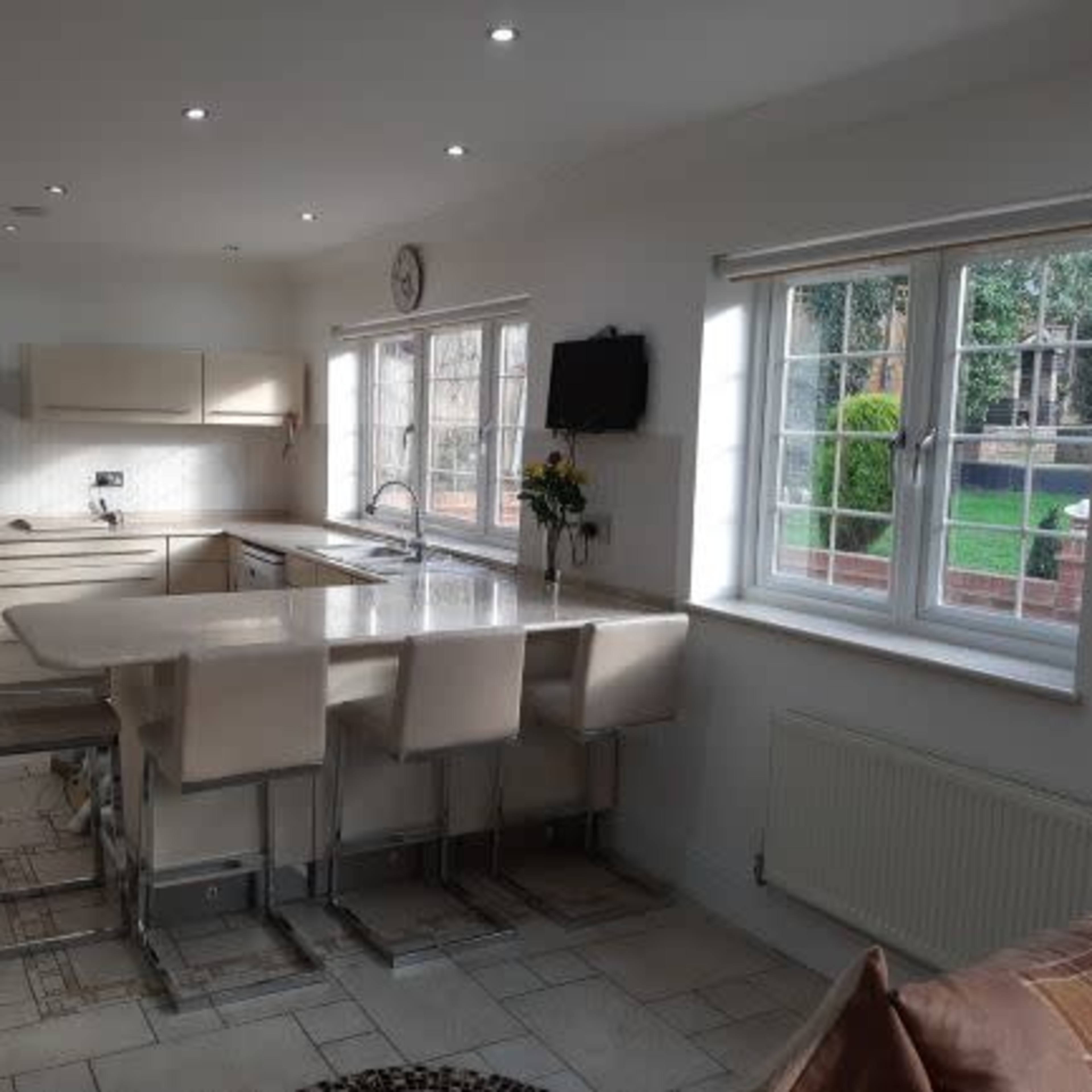 A modern kitchen features a central island with seating, white cabinetry, and large windows overlooking a garden.