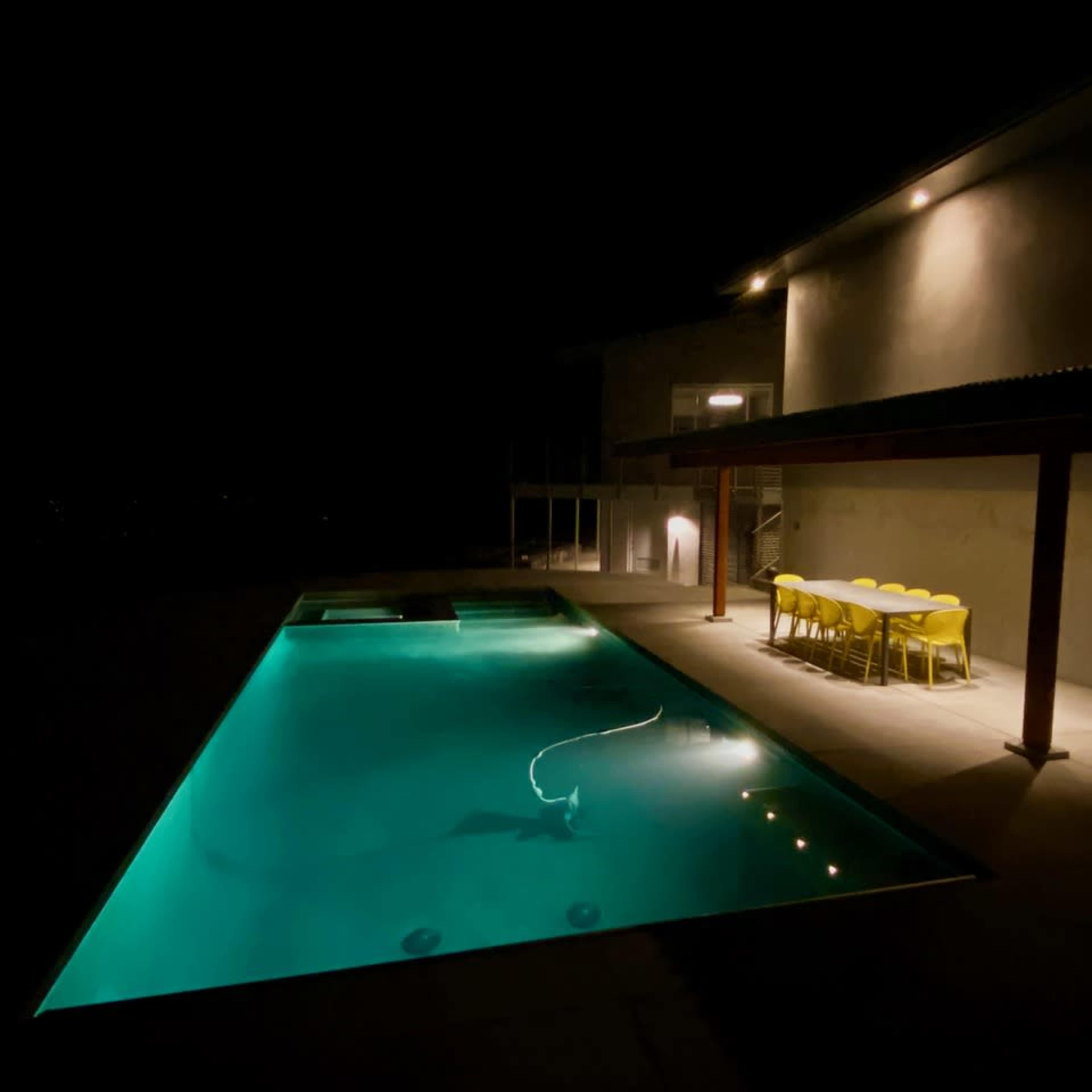 A modern house with a swimming pool and dining area is illuminated at night.