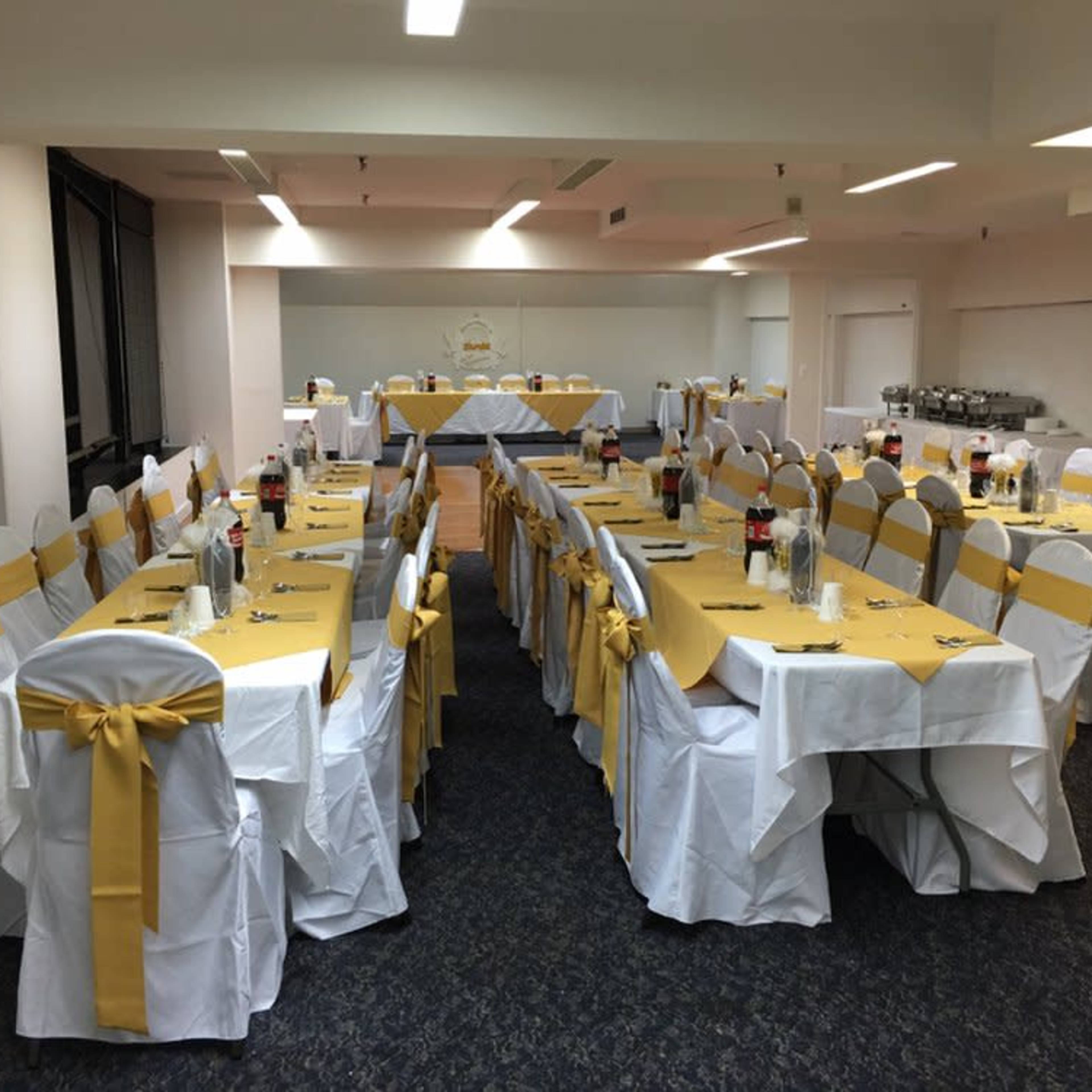 A banquet room is set up with a long rectangular table dressed in white and burgundy, surrounded by neatly arranged chairs.