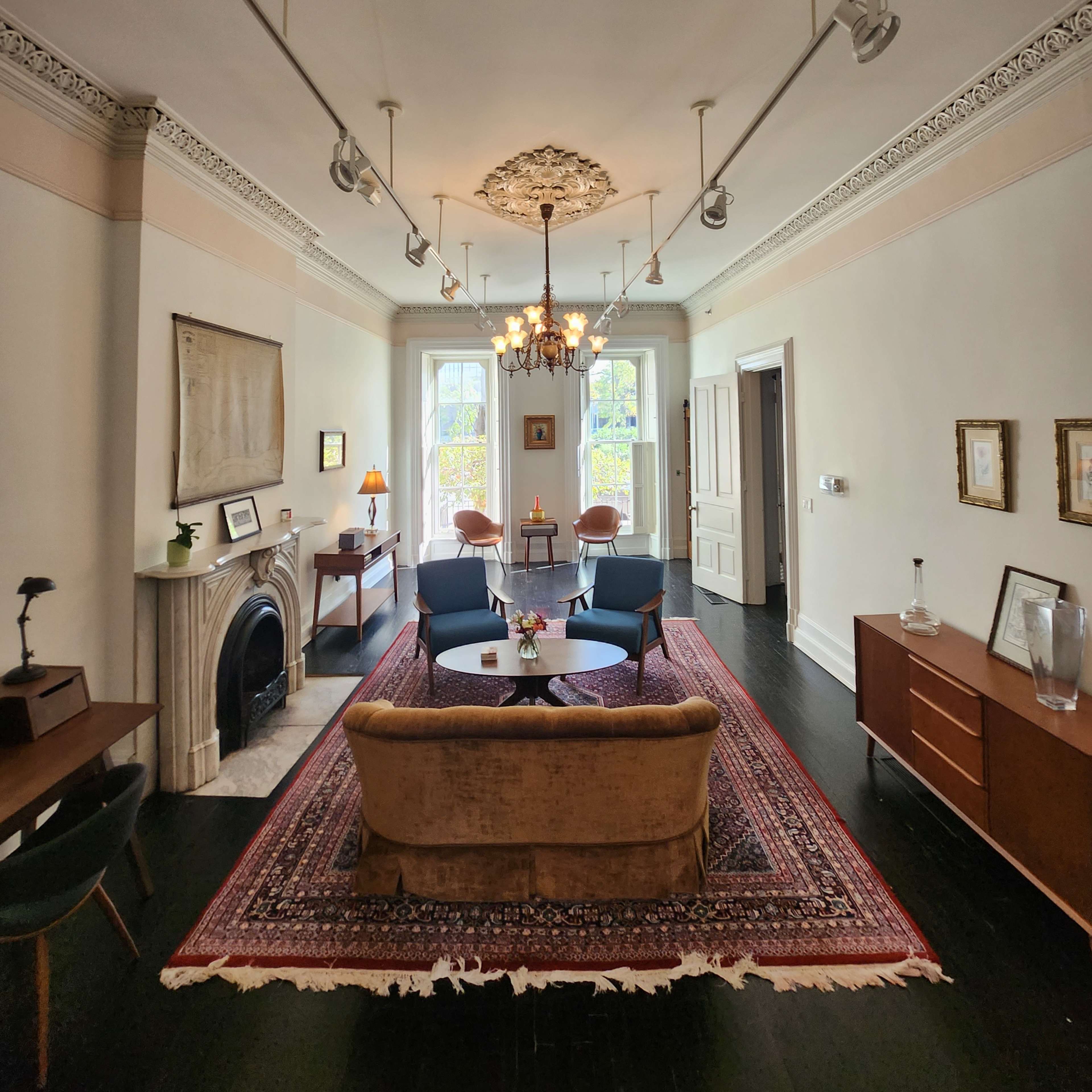 A spacious living room featuring a central chandelier, a patterned area rug, and a fireplace with modern furniture arranged around it.