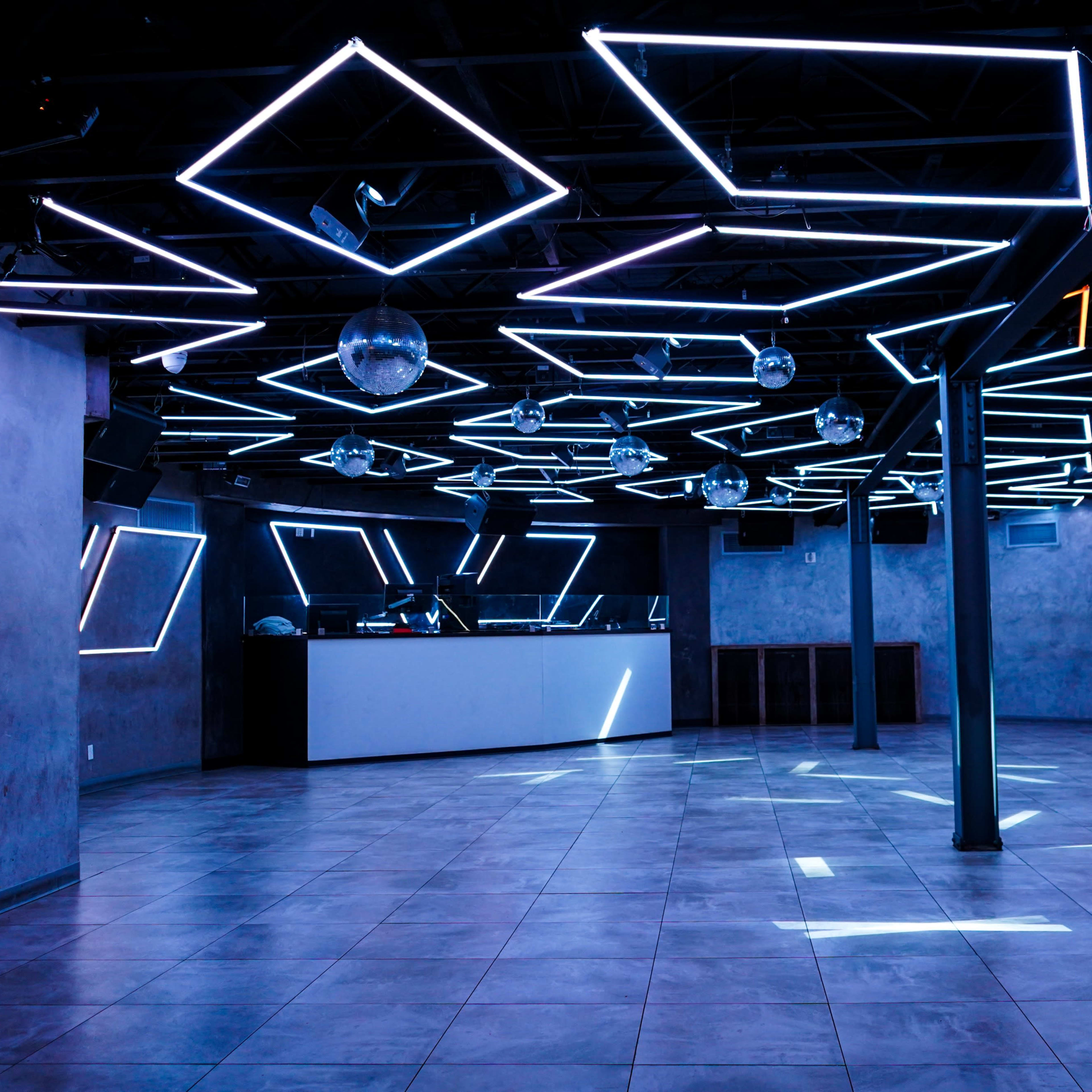 A modern dance club interior featuring geometric LED lights on the ceiling and a sleek bar area in the background.