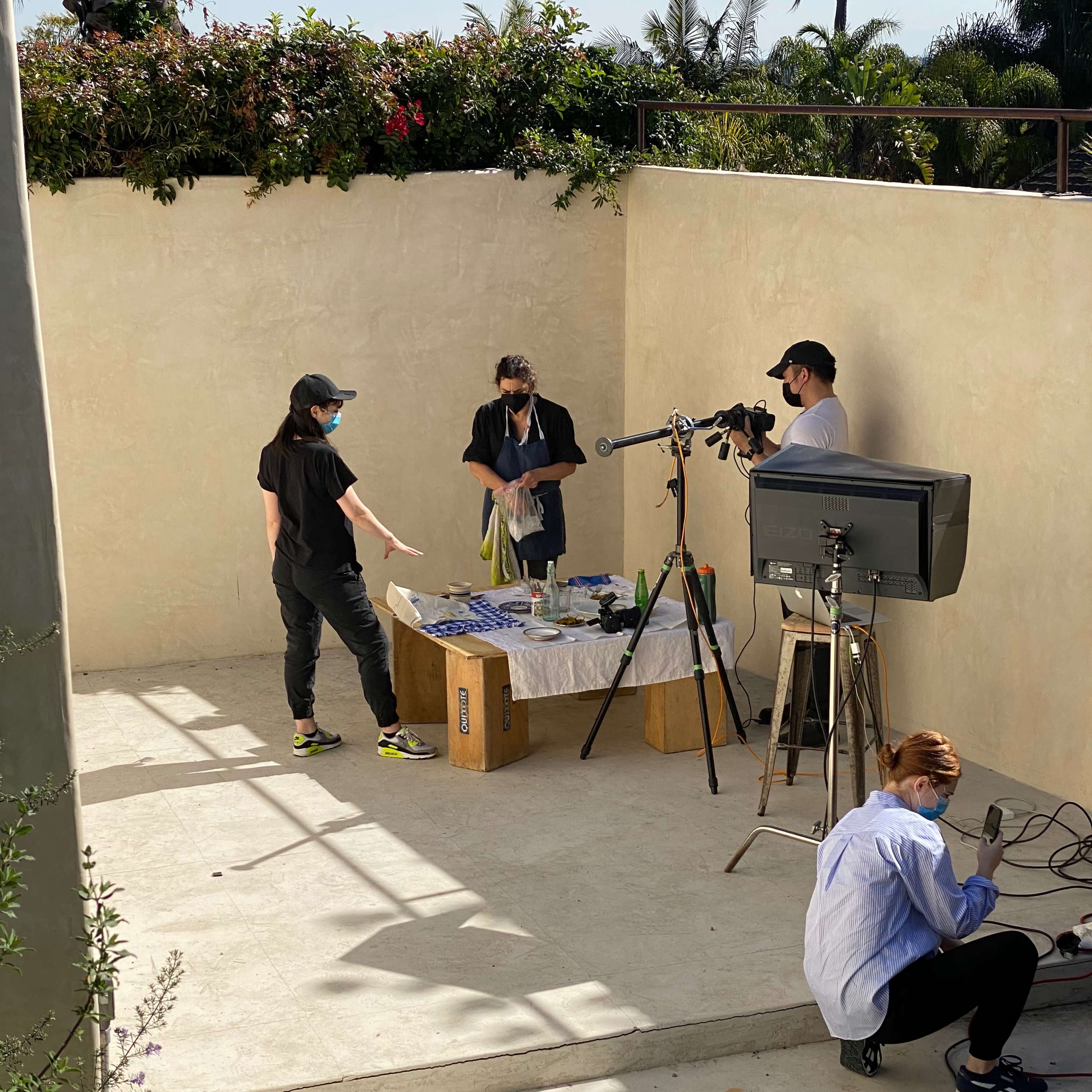 A group of four people sets up a video shoot in an outdoor space with a table and camera equipment.
