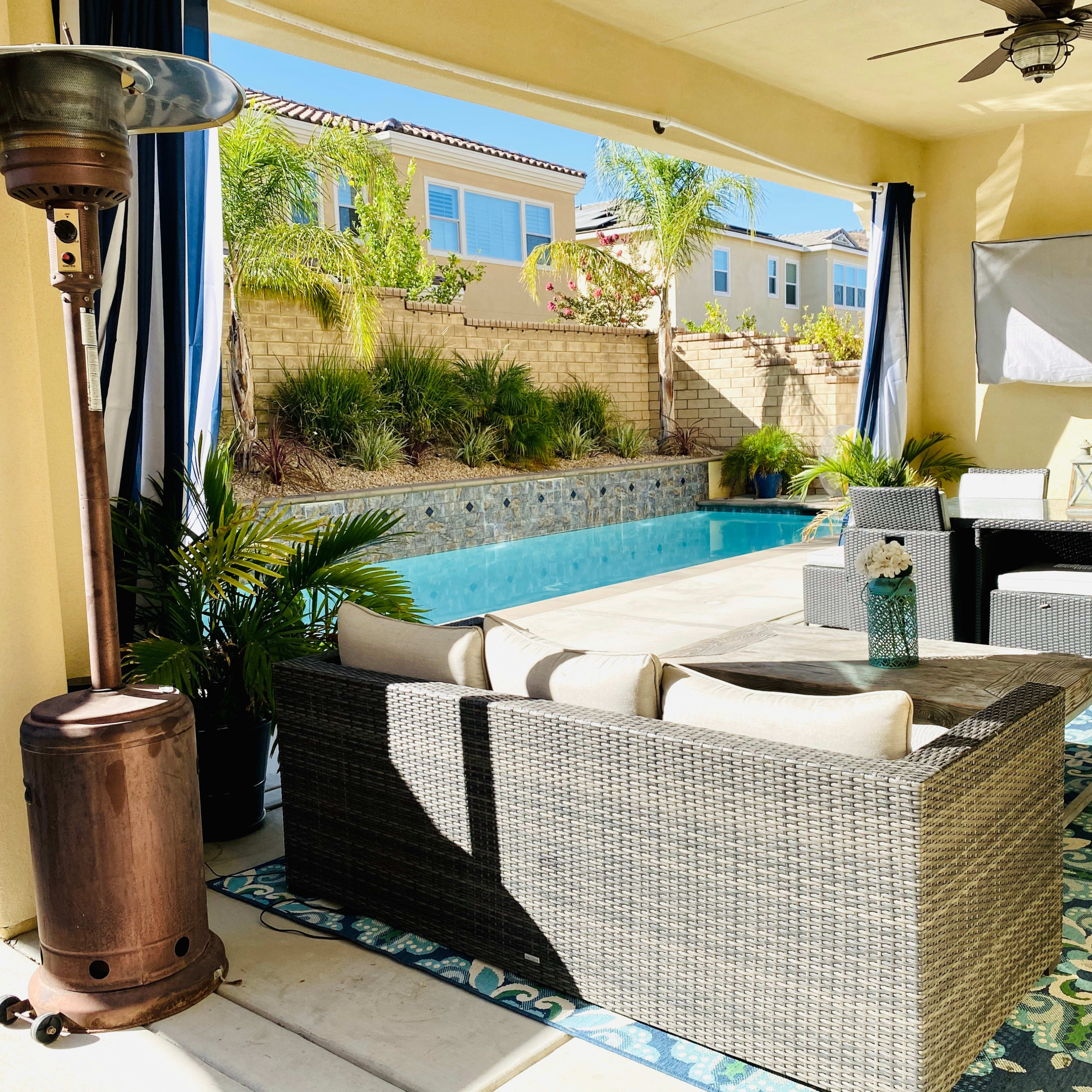 A patio area with a pool in the background, featuring outdoor furniture and a heater.