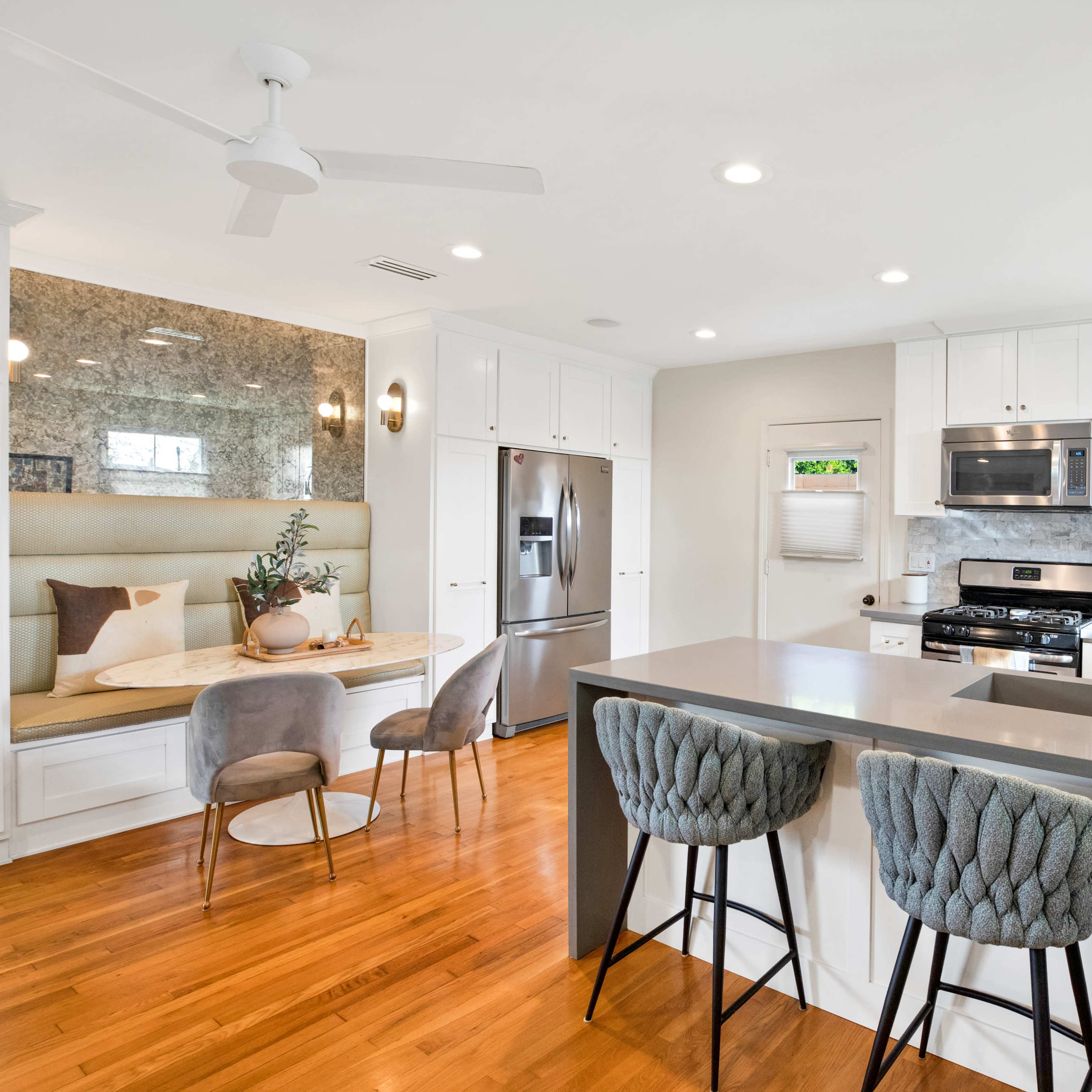 A modern kitchen features white cabinets, stainless steel appliances, a large island with bar stools, and a cozy nook with seating.