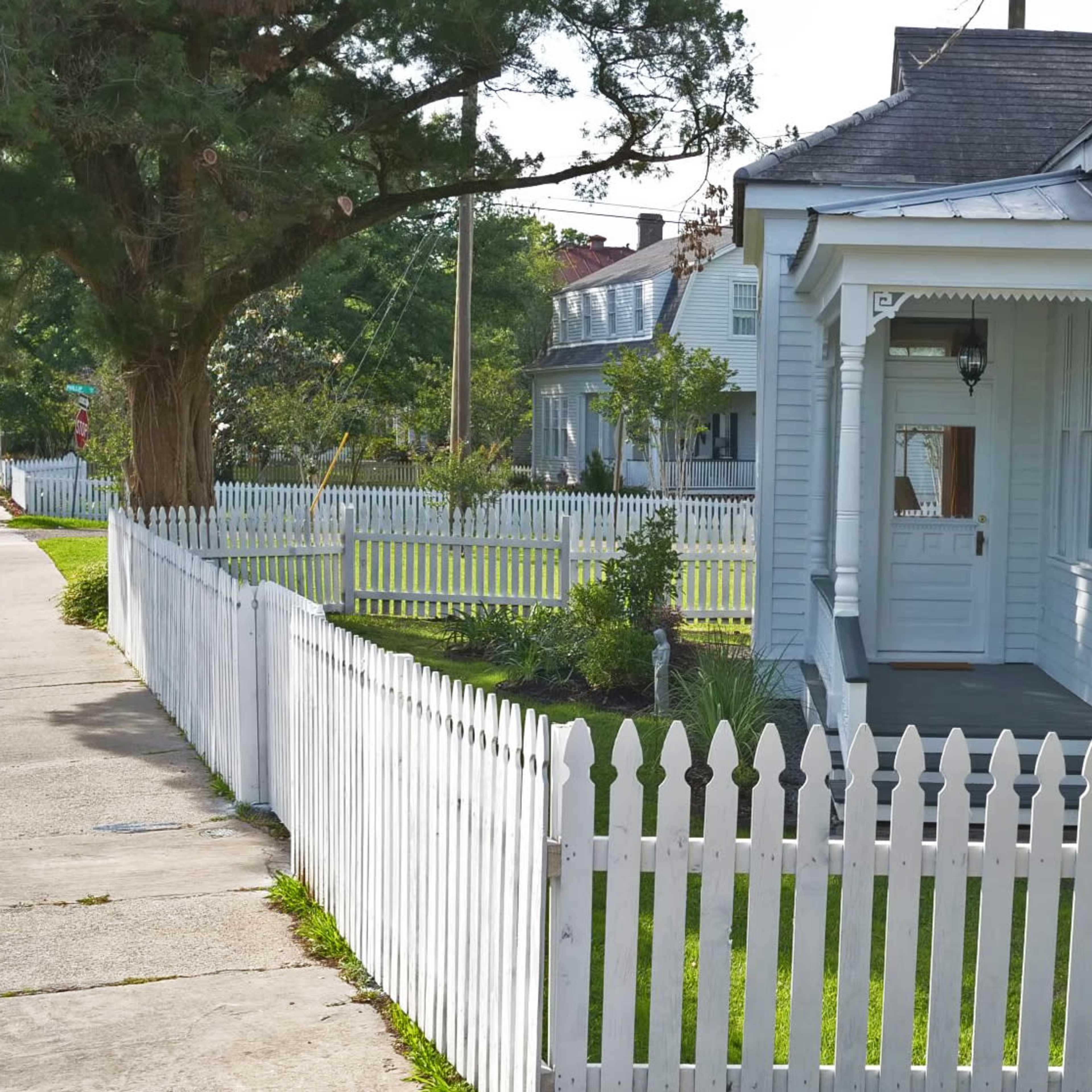 A white picket fence surrounds a small house with a porch and a neatly landscaped yard.