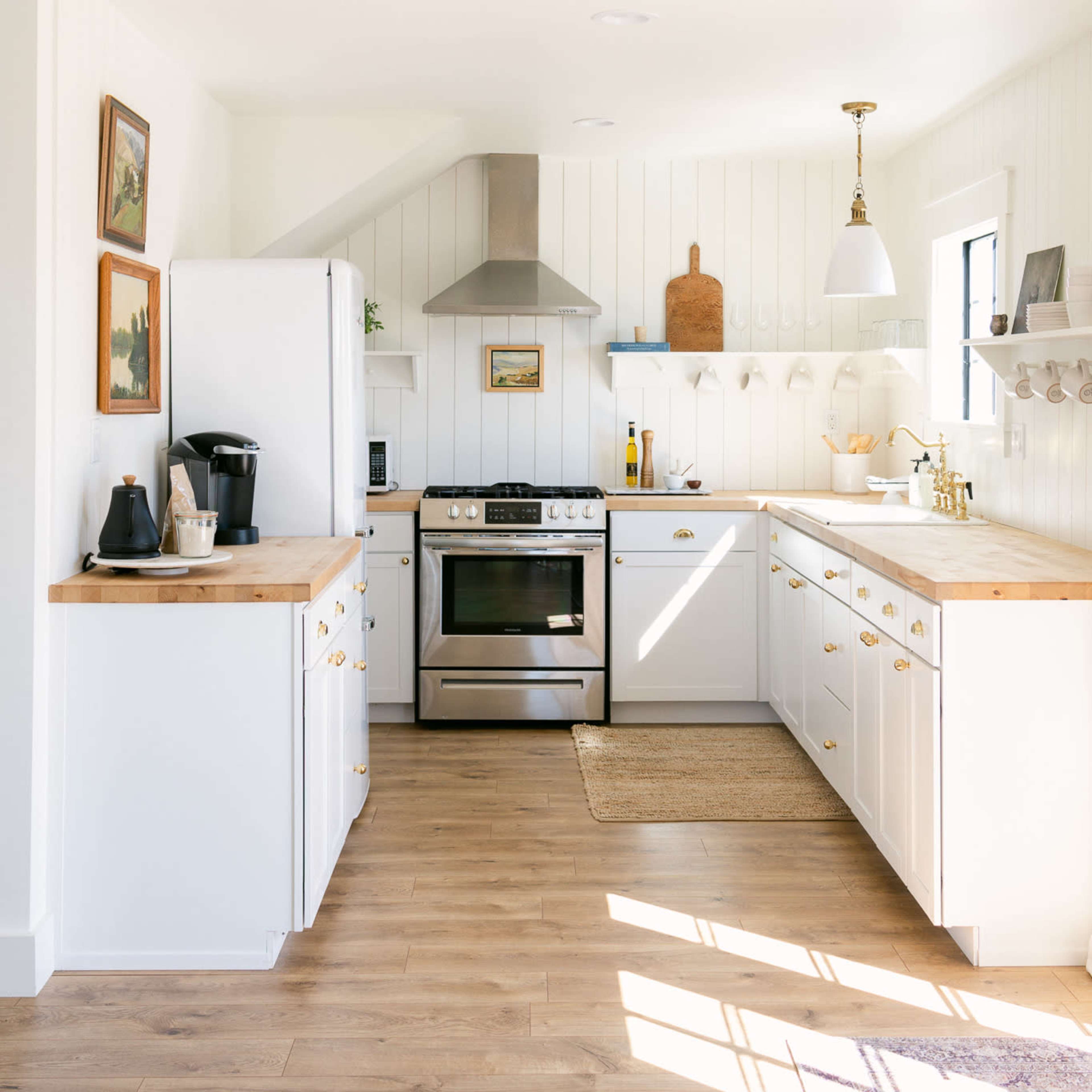 A bright kitchen features white cabinetry, a stainless steel stove, a large refrigerator, and wooden countertops, with various decorative items on display.