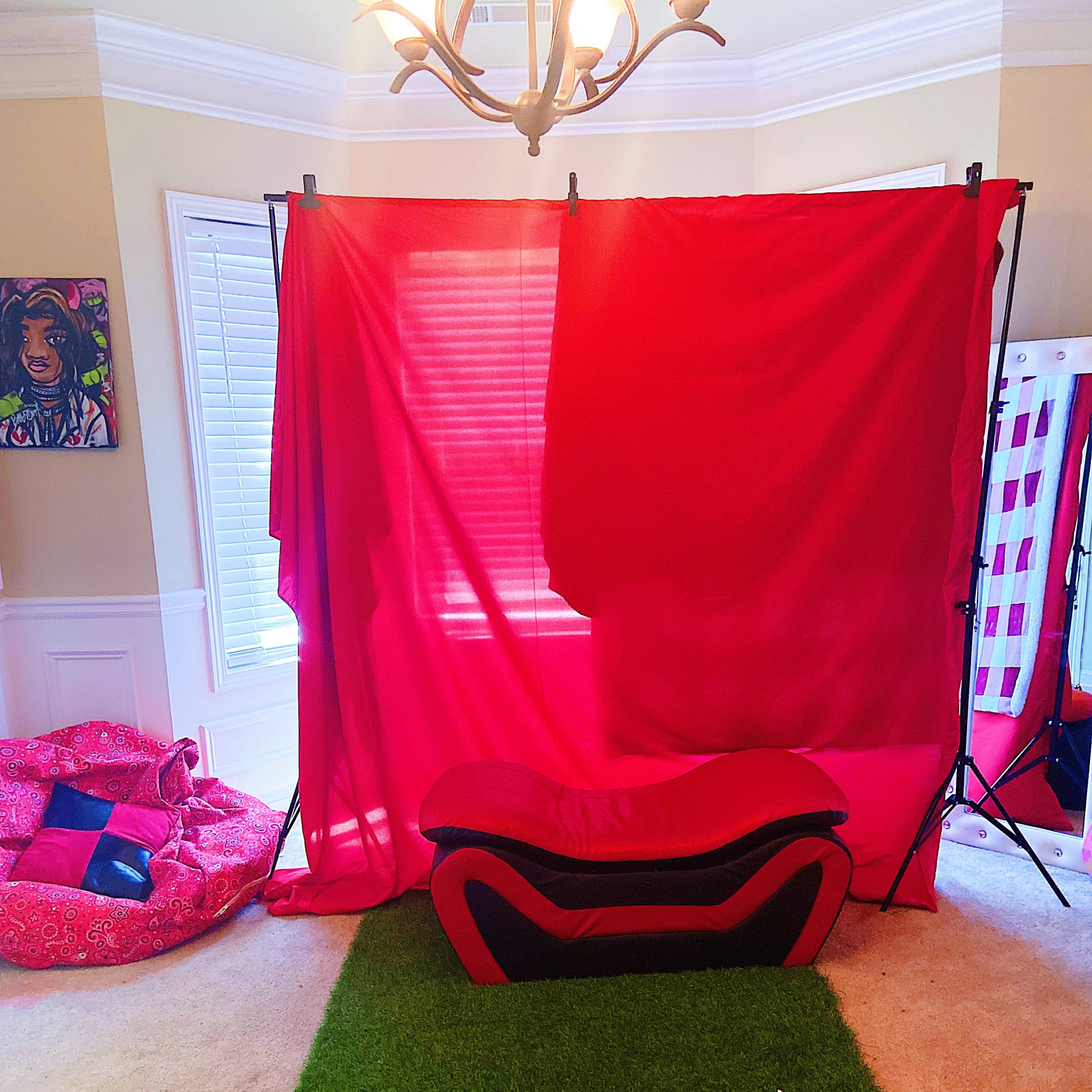 A room with a red backdrop set up, a black and red couch in front, and a green carpet on the floor.