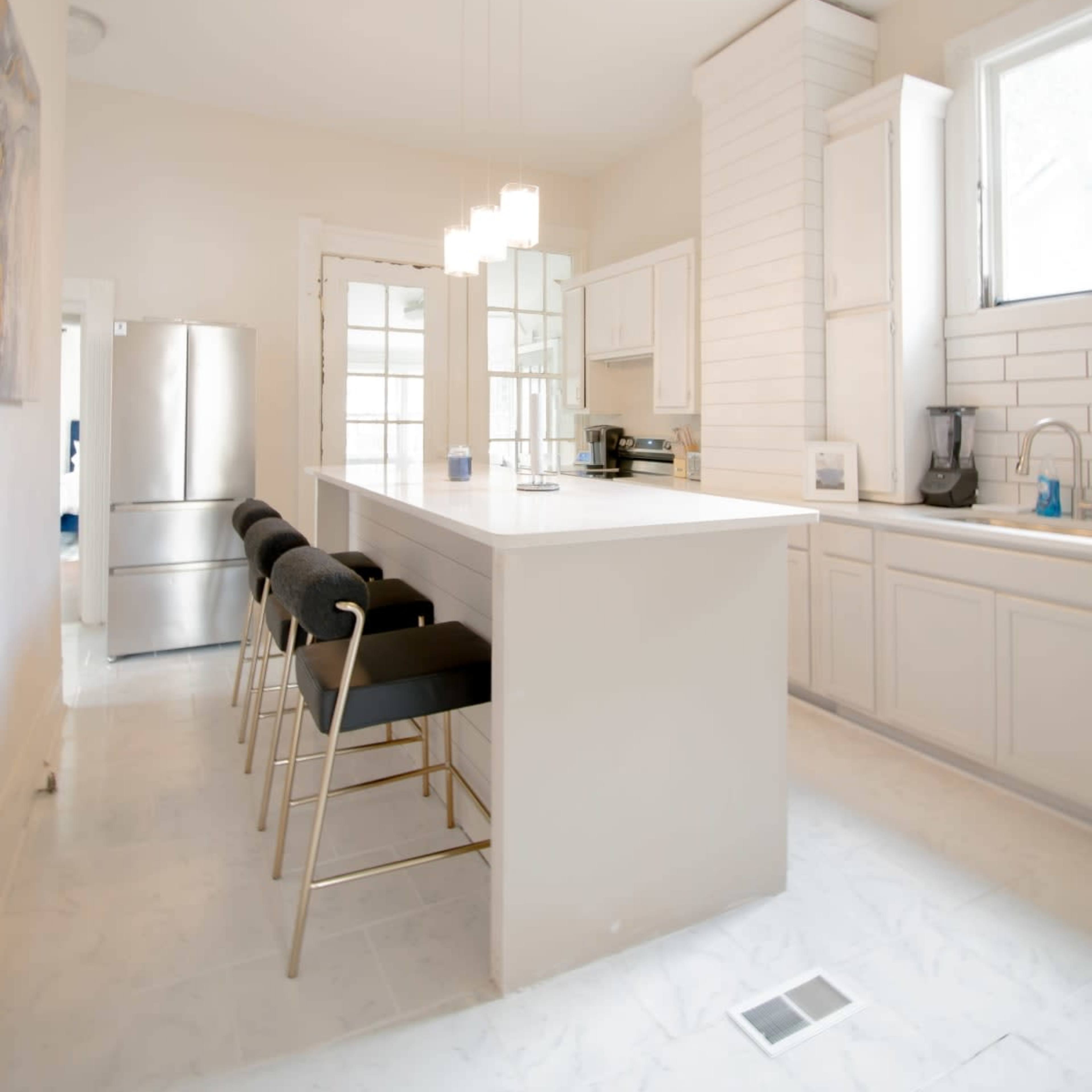 A modern kitchen features white cabinetry, a large island with bar stools, and stainless steel appliances.