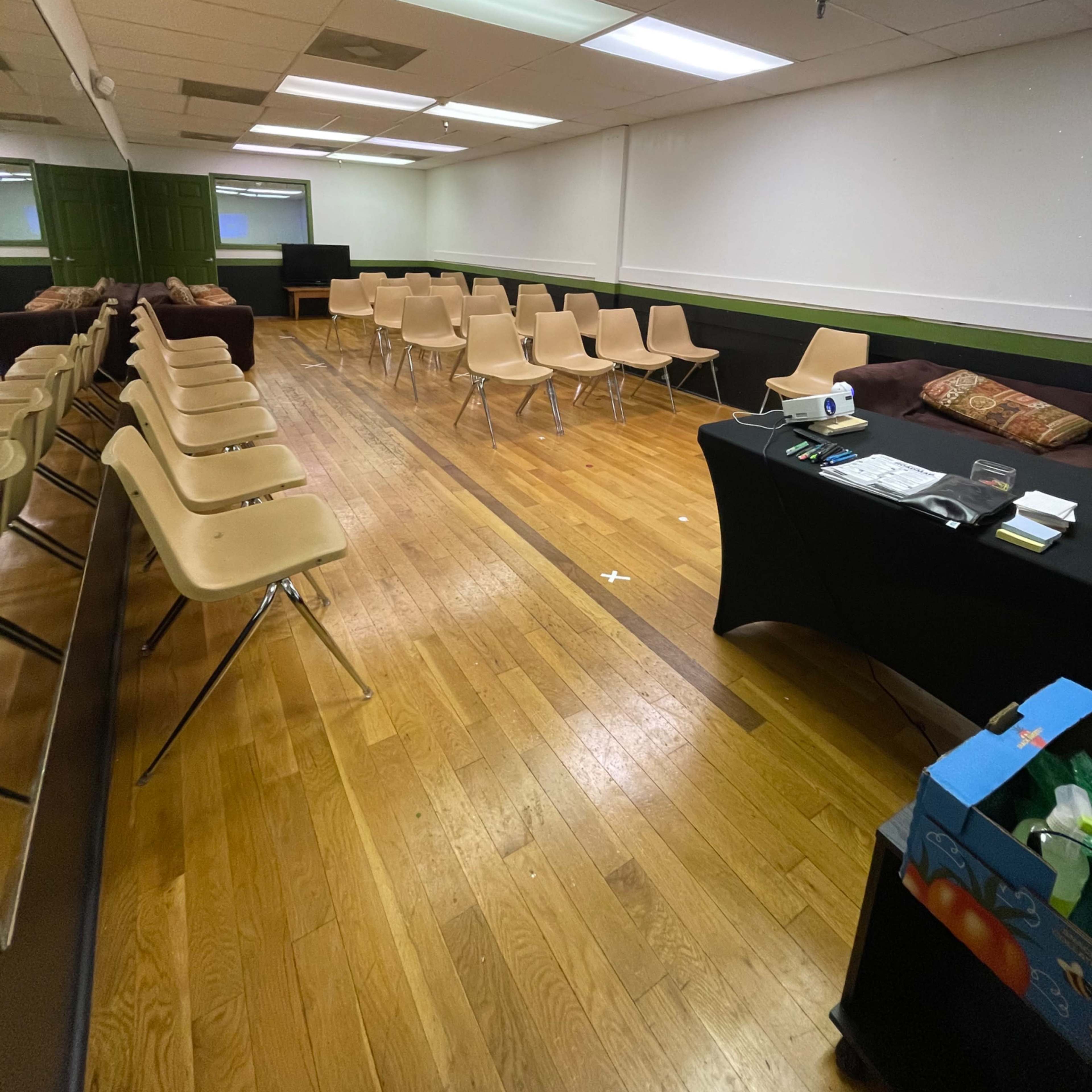 A sparsely furnished room with rows of empty chairs and a table at the side, featuring a roll of paper and a box.