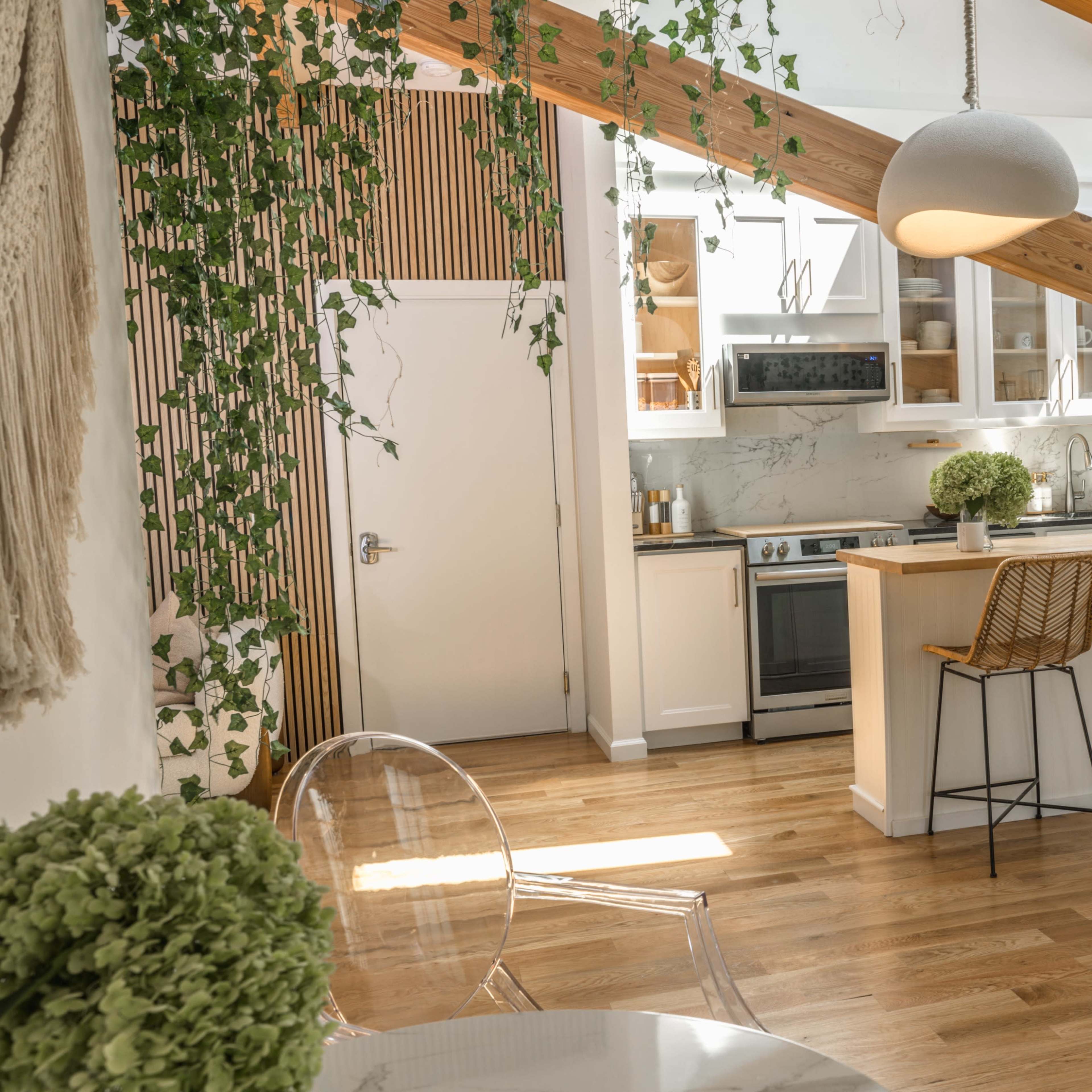 A modern kitchen with wooden beams, white cabinetry, and bar stools, accented by greenery and natural light.