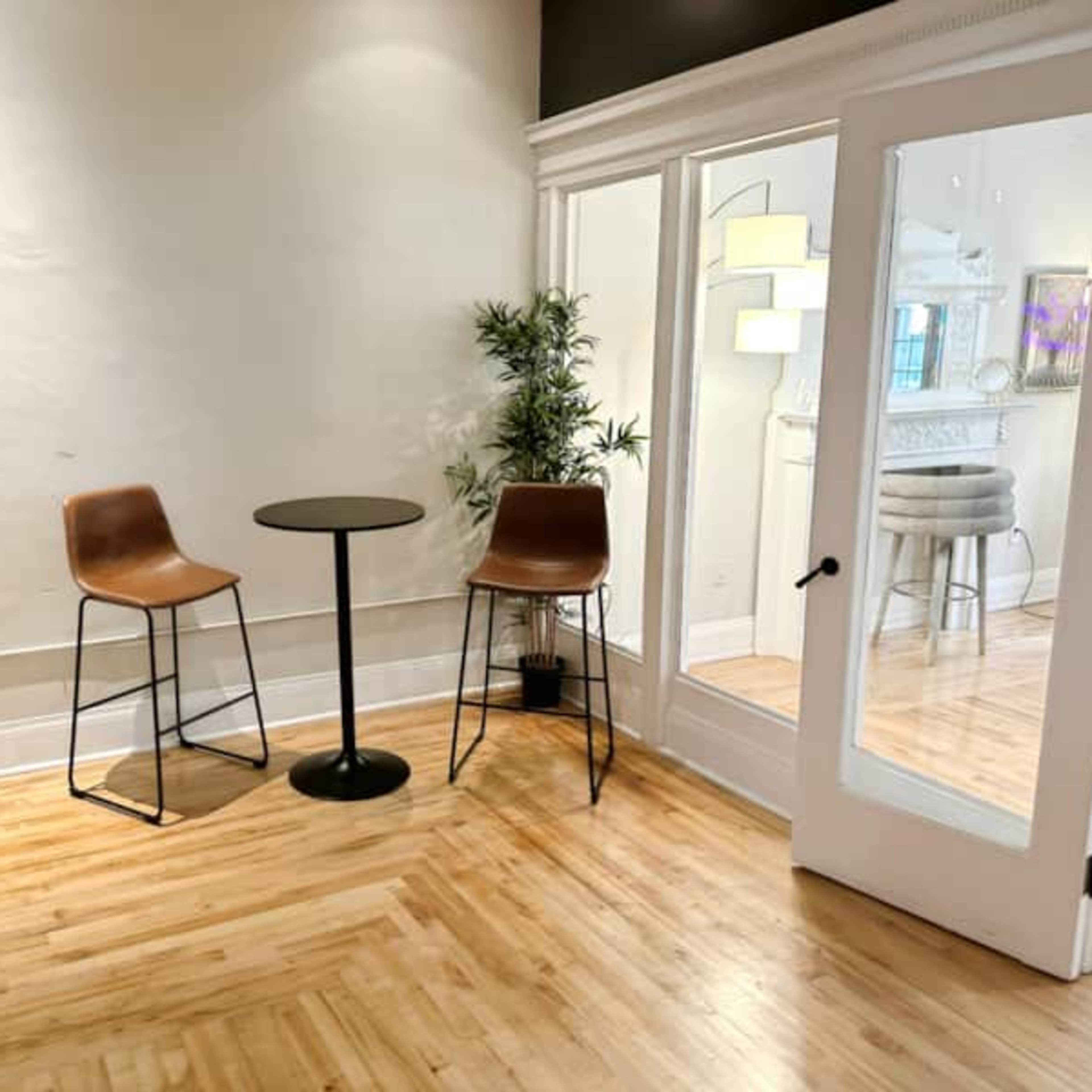 A small room features a round table with two high chairs and a potted plant, adjacent to a glass-paneled door leading to another space.