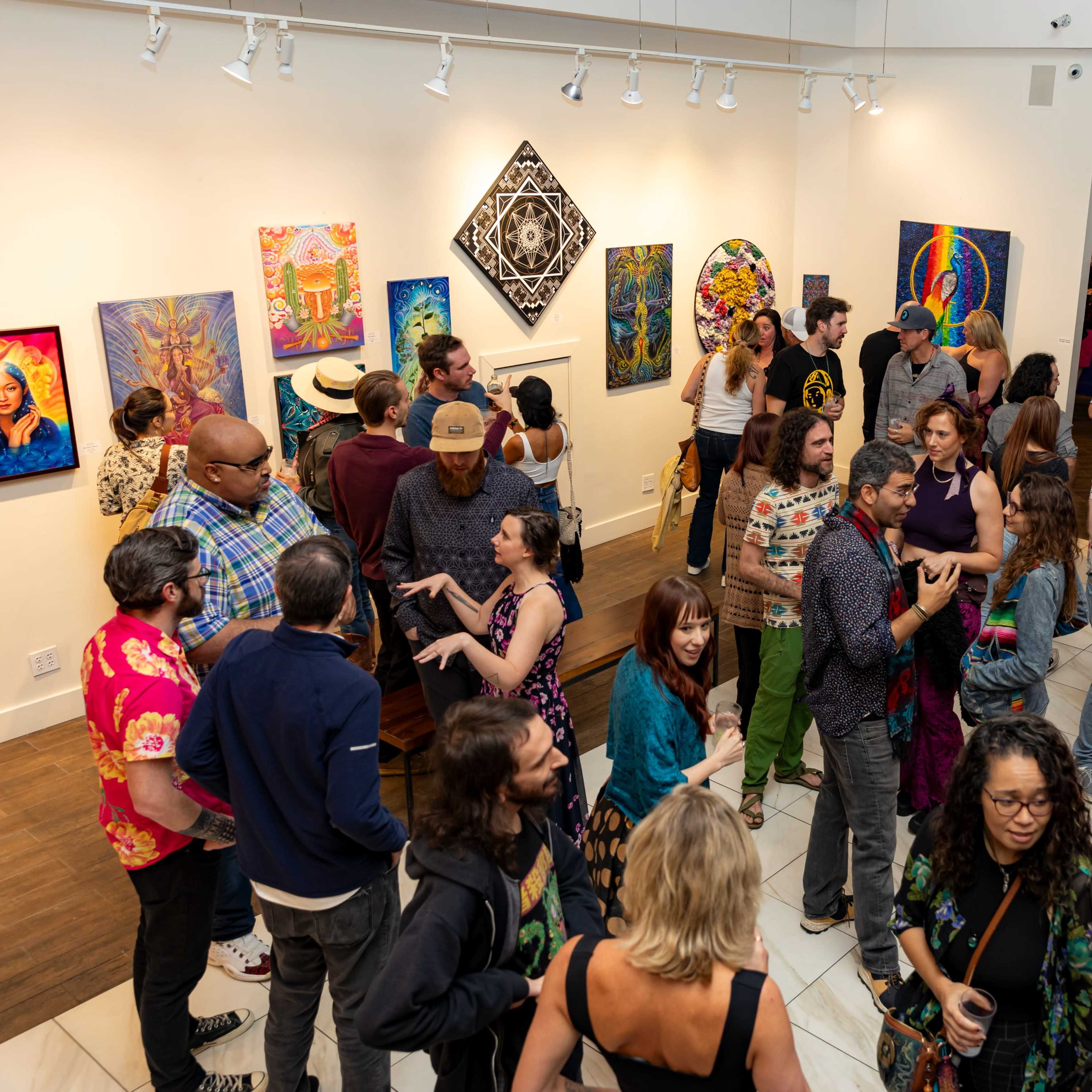 A diverse group of people gathers in an art gallery filled with colorful paintings on the walls.