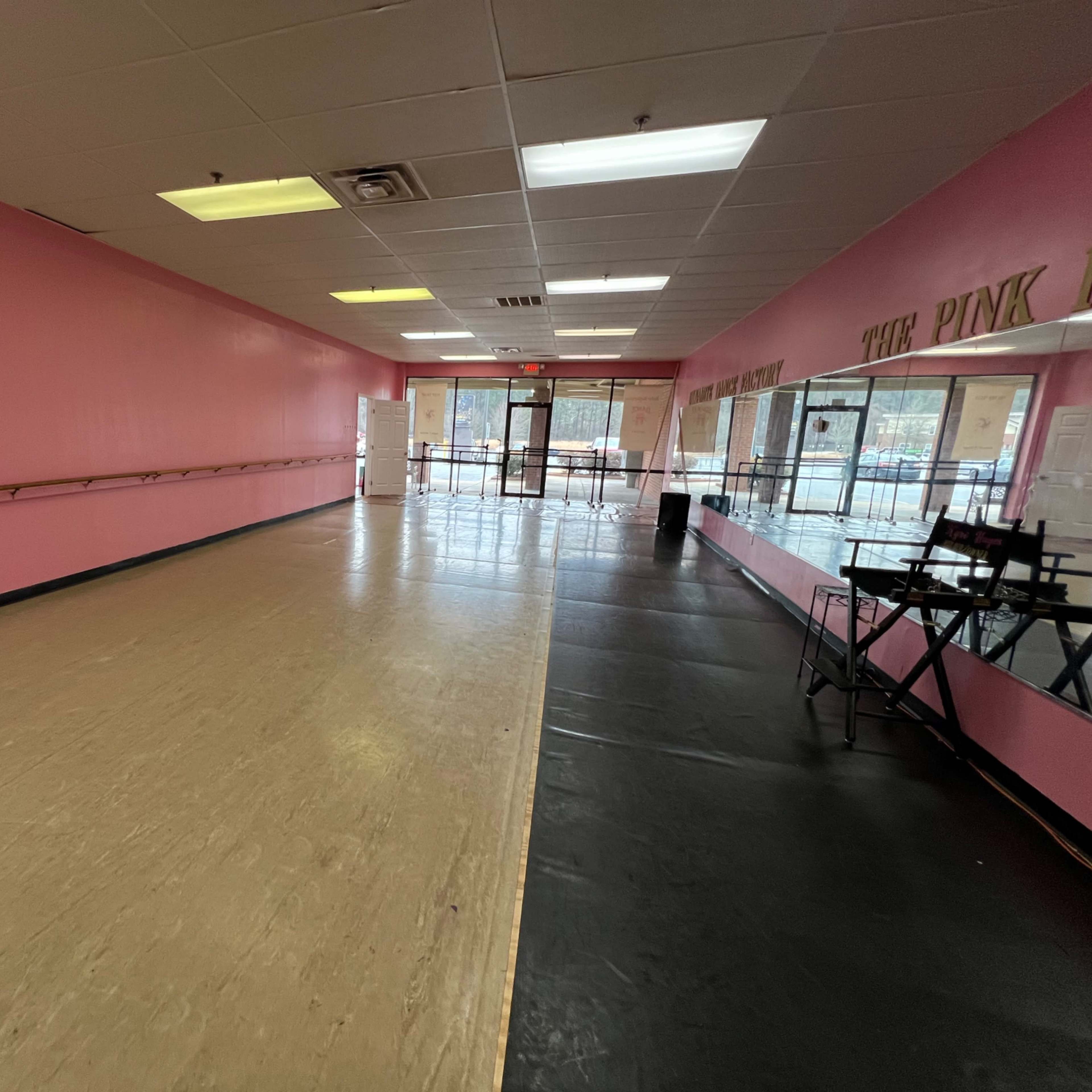 A dance studio with pink walls, a wooden floor, and a dance barre along one side.