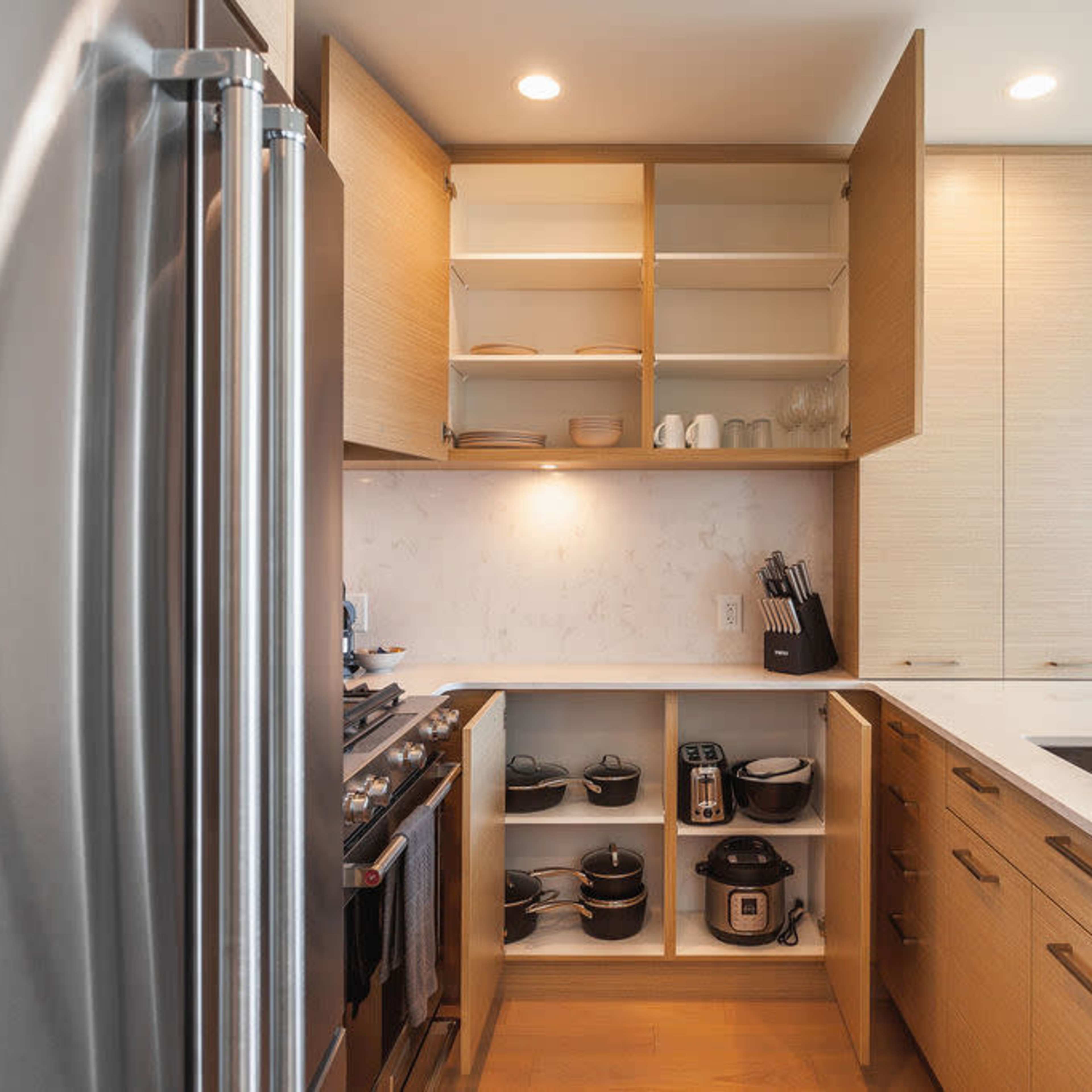 A modern kitchen with light wood cabinetry, open shelves, a stainless steel fridge, and various kitchen appliances neatly organized.