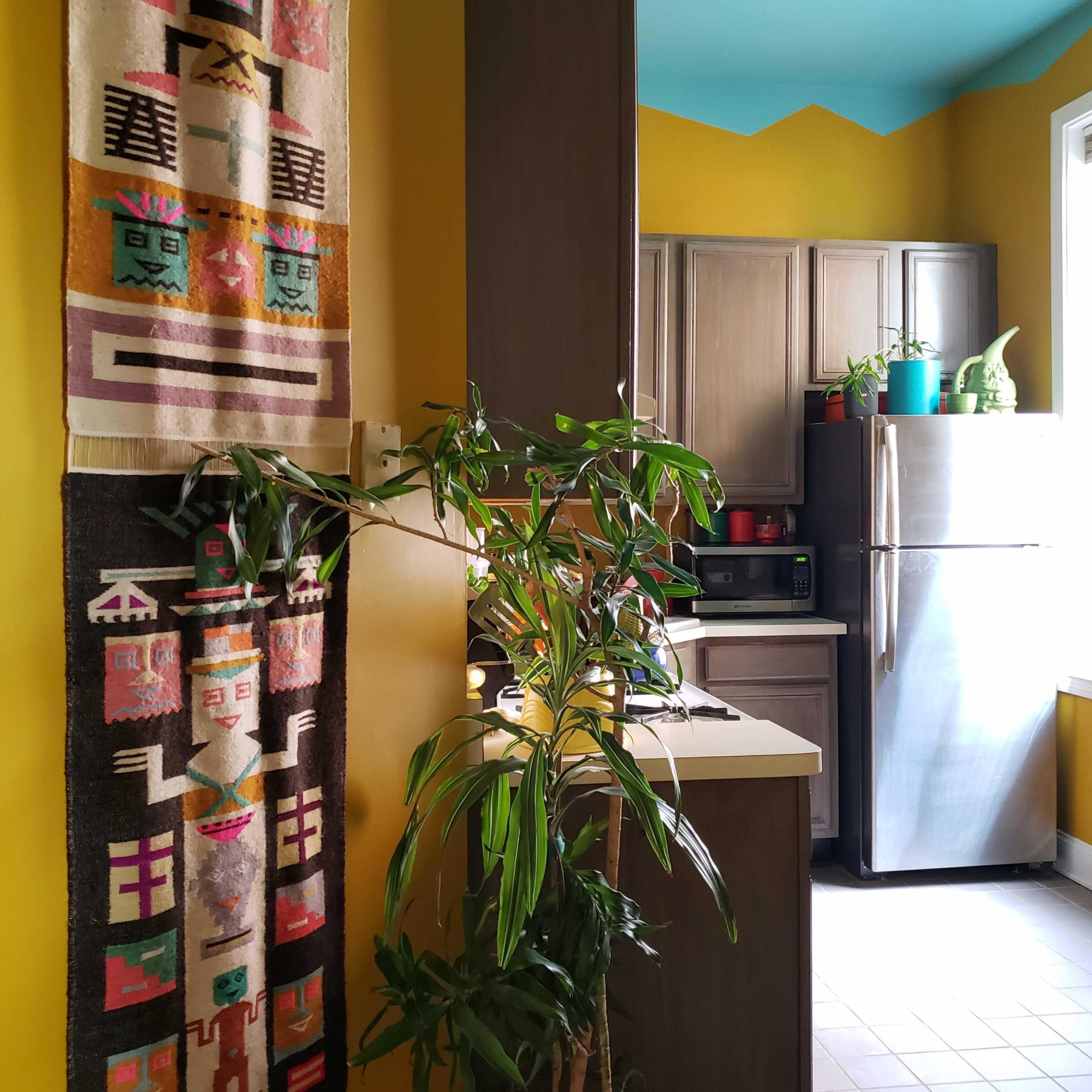 A brightly colored kitchen features ethnic wall hangings, plants, and modern appliances.