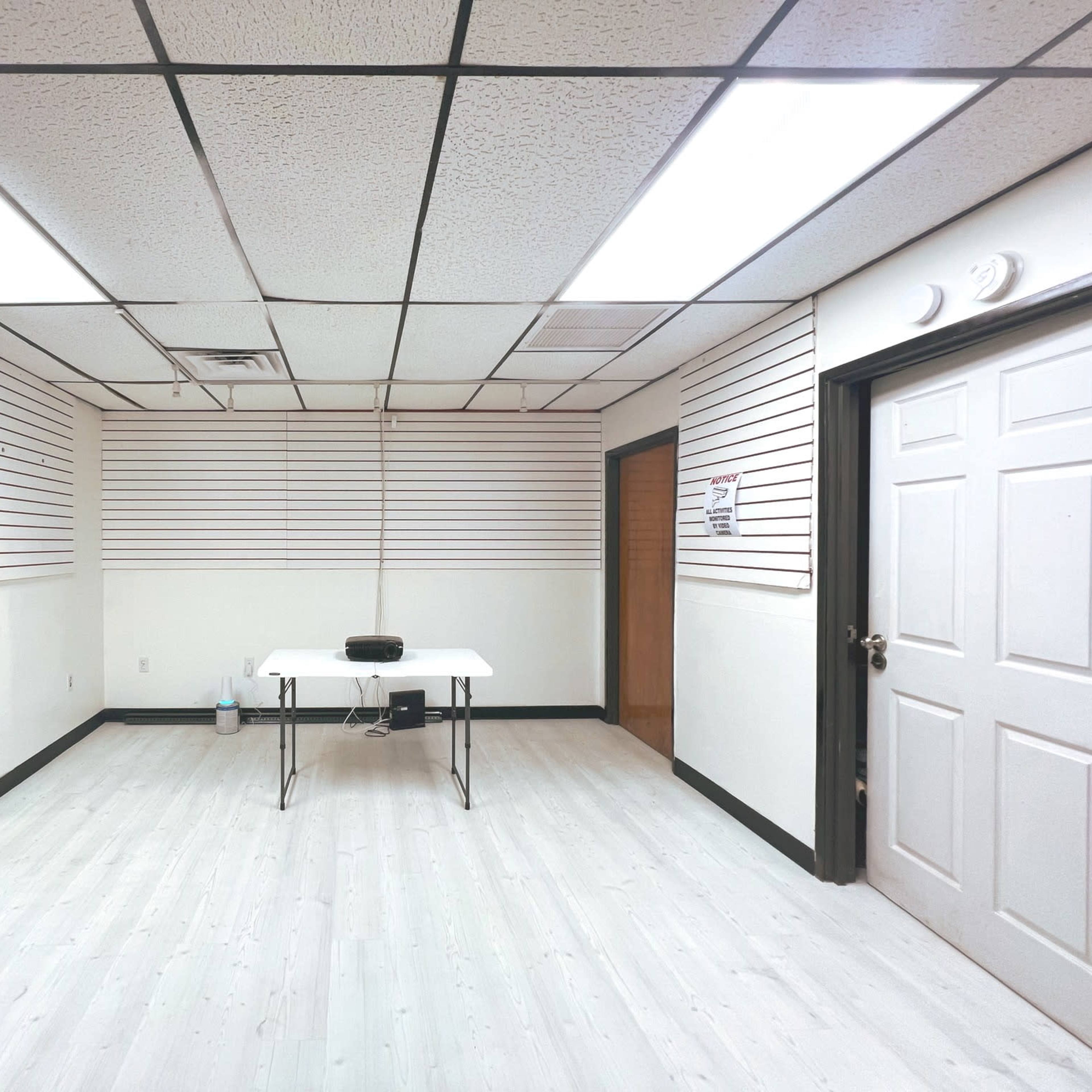 An empty room with a table in the center, white walls, and a door on the right side.