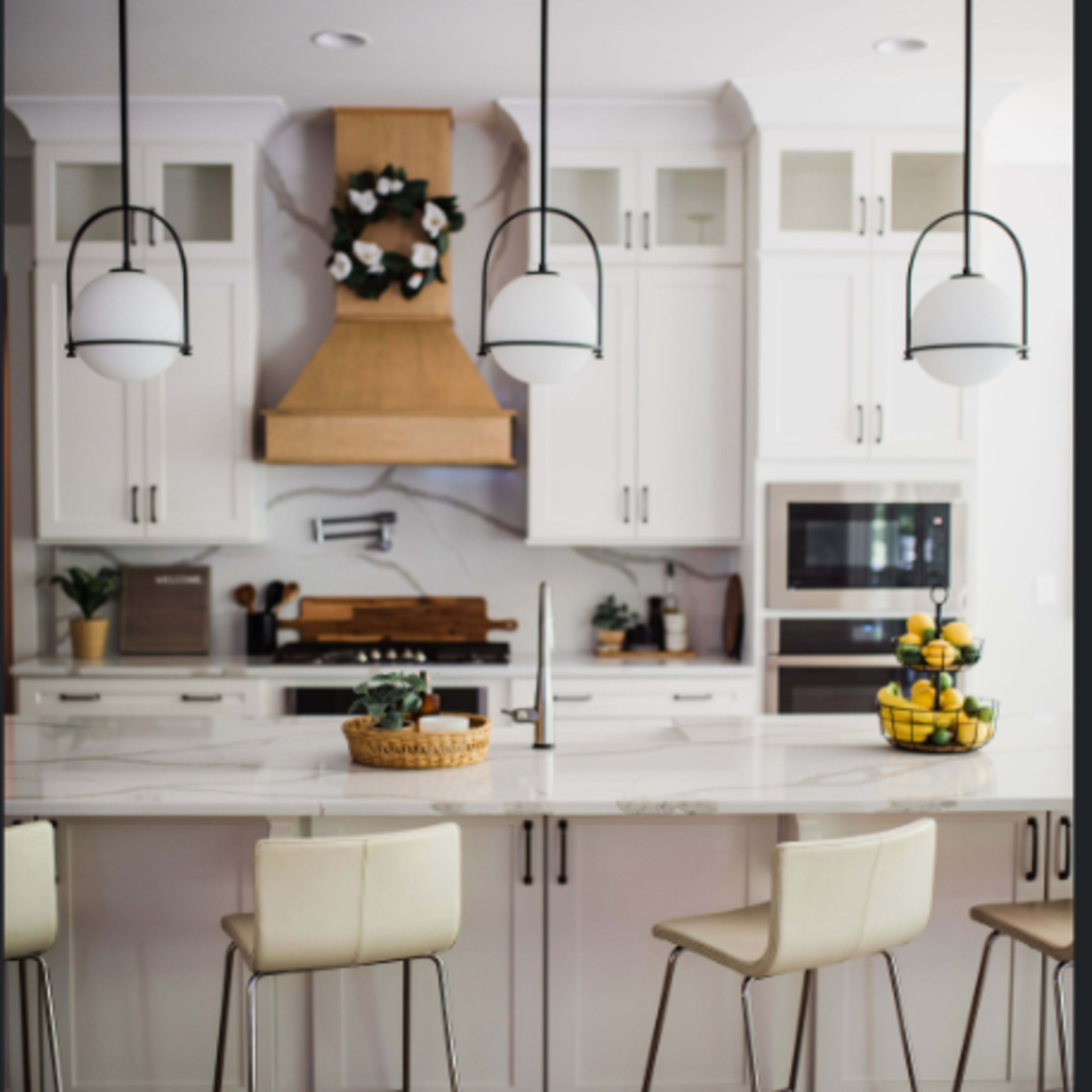 A modern kitchen with white cabinetry, a large island featuring four bar stools, and a wooden range hood above the stove.
