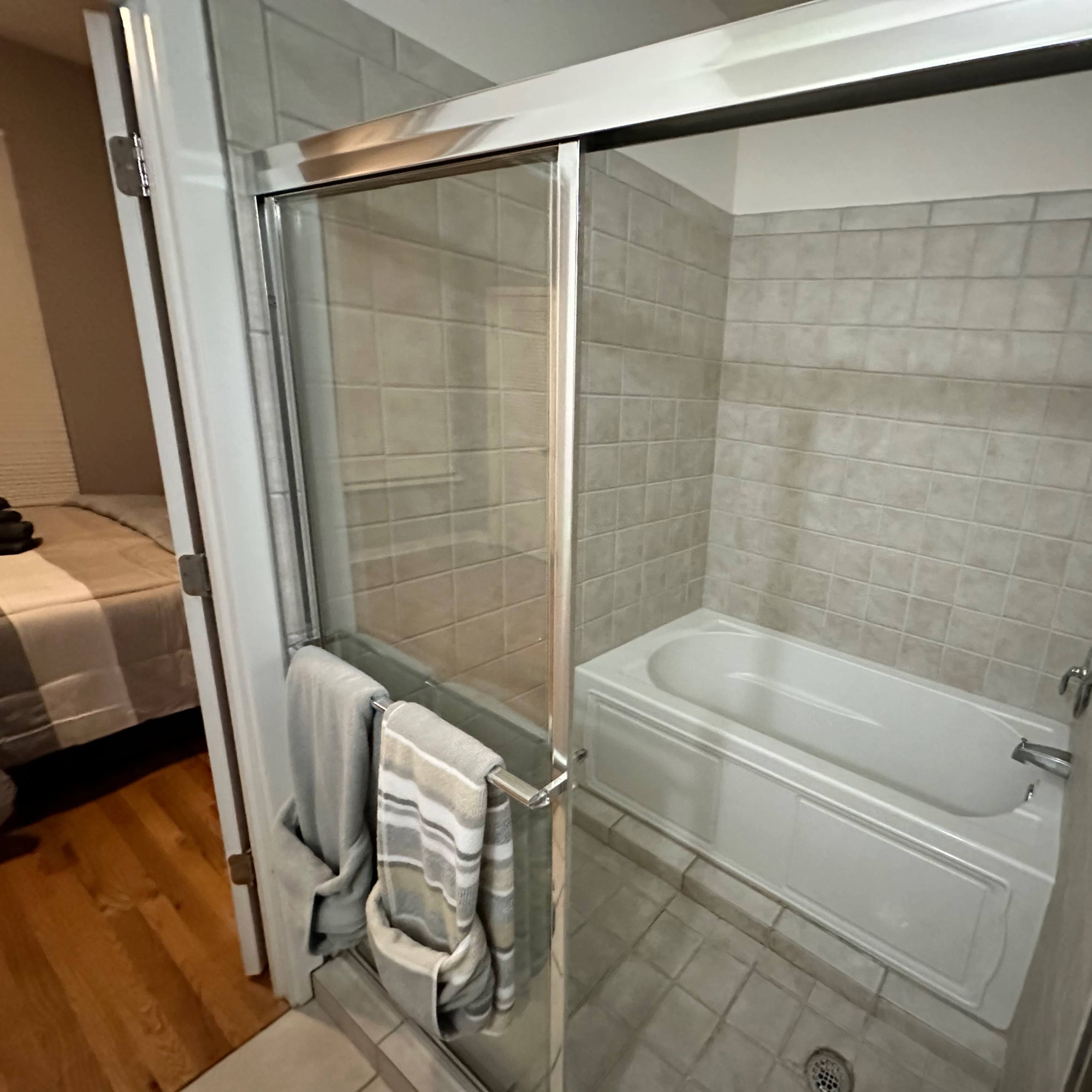 A bathroom with a glass shower enclosure and a bathtub, featuring tiled walls and a wooden floor.