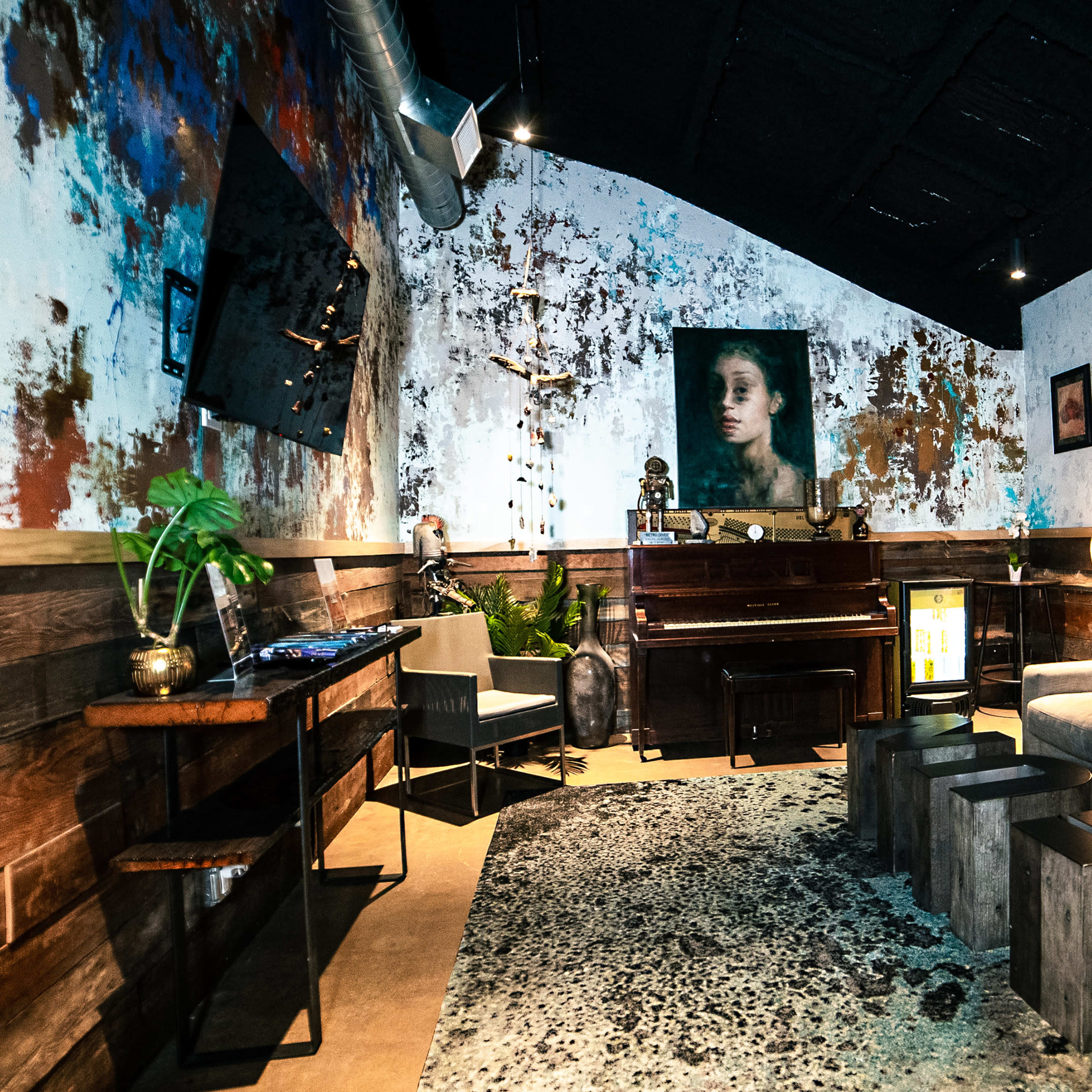 A cozy lounge area with a piano, artwork on the walls, and a sofa arranged around a textured rug.