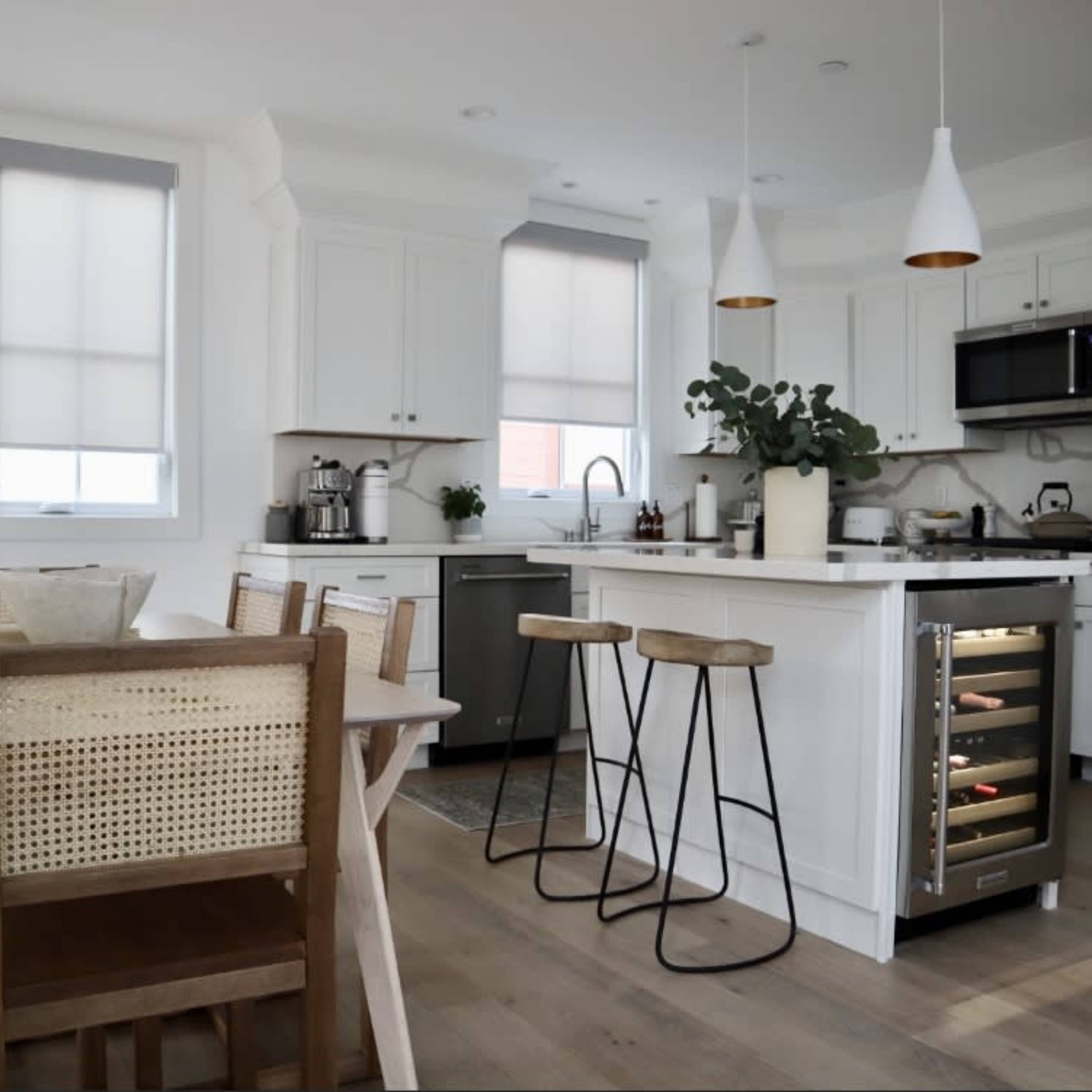 A modern kitchen features white cabinetry, stainless steel appliances, a central island with bar stools, and a dining table set for several people.