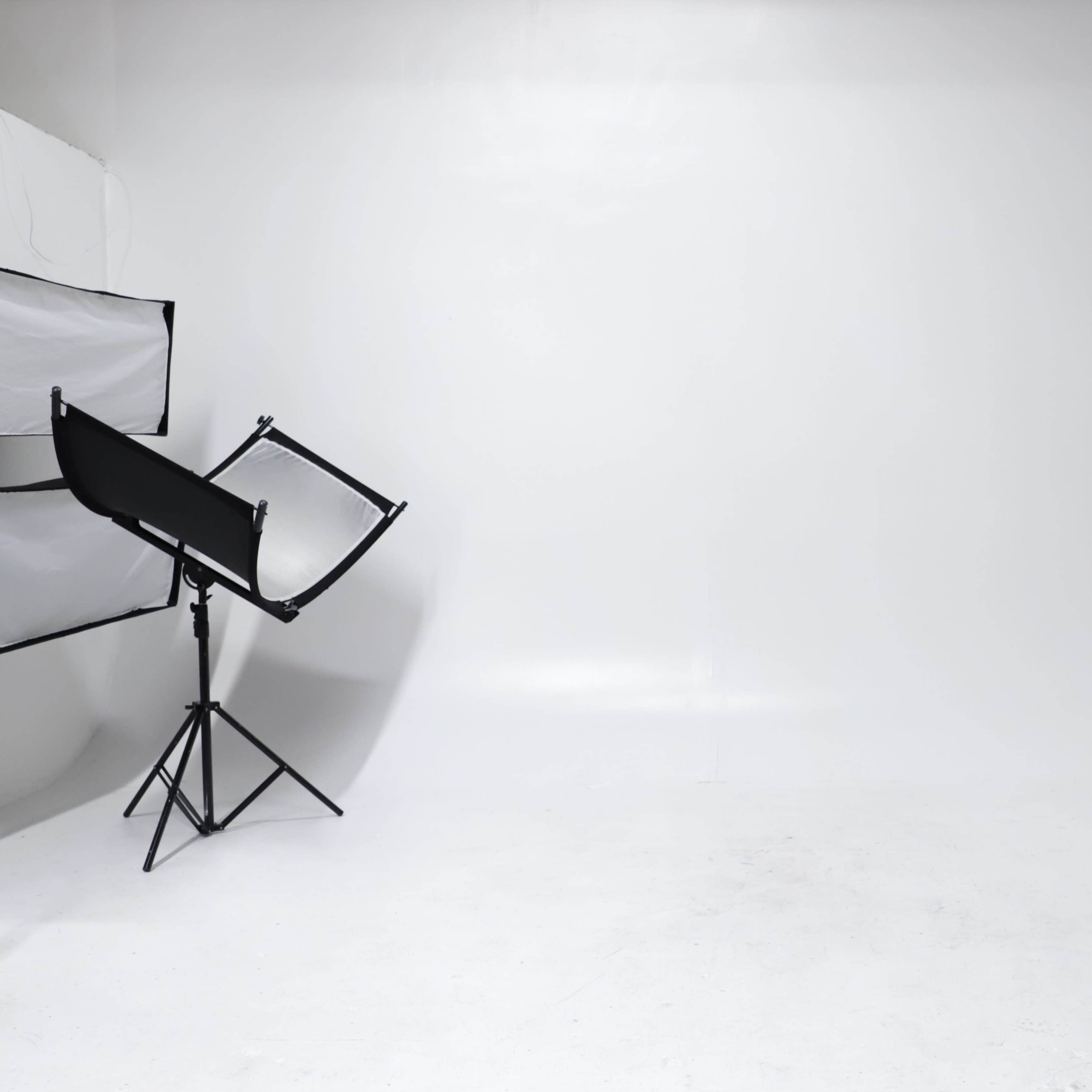A minimalist photo studio with a large blank white backdrop, a light stand, and a set of white steps in the corner.