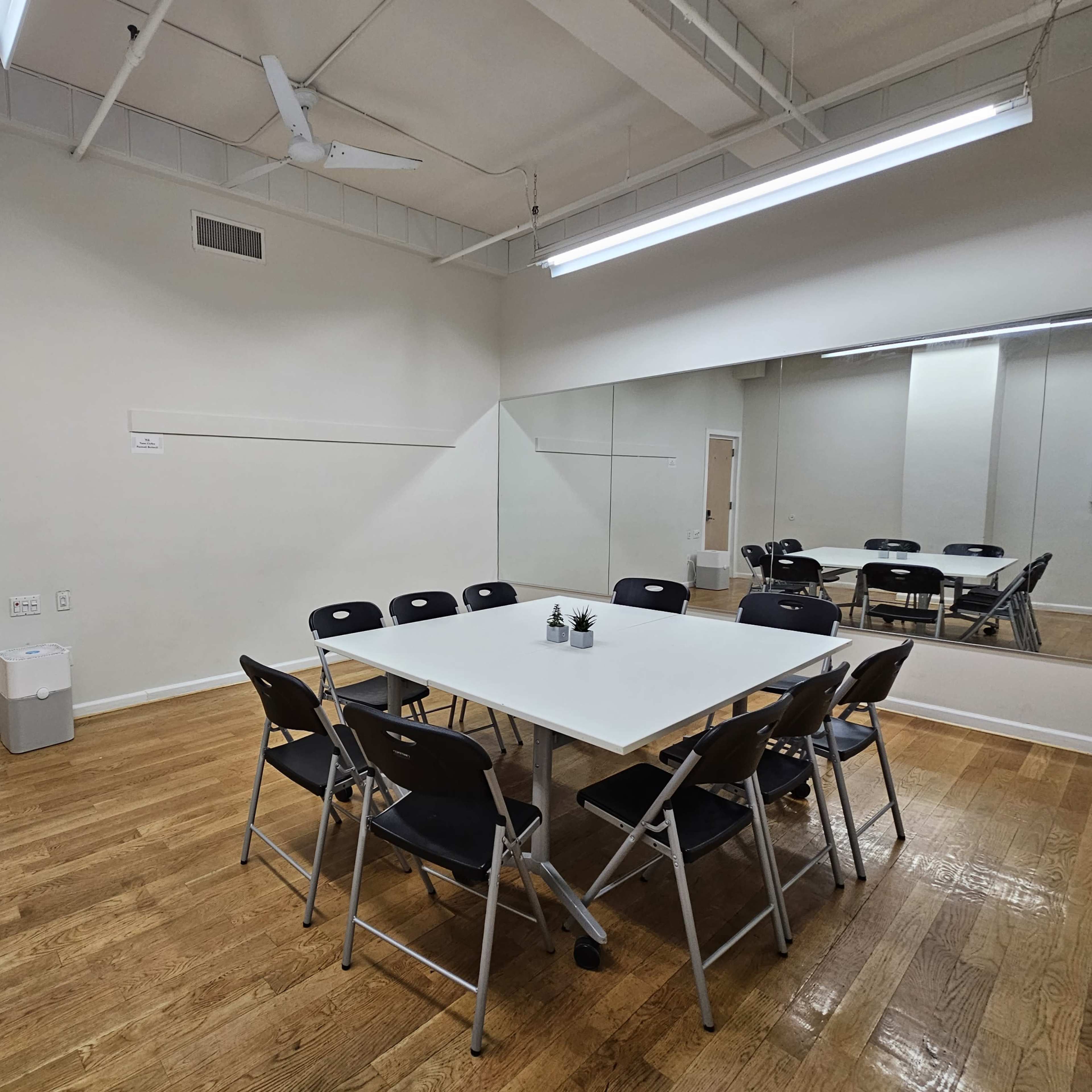 A meeting room features a large table surrounded by folding chairs, with a door and a mirror on adjacent walls.