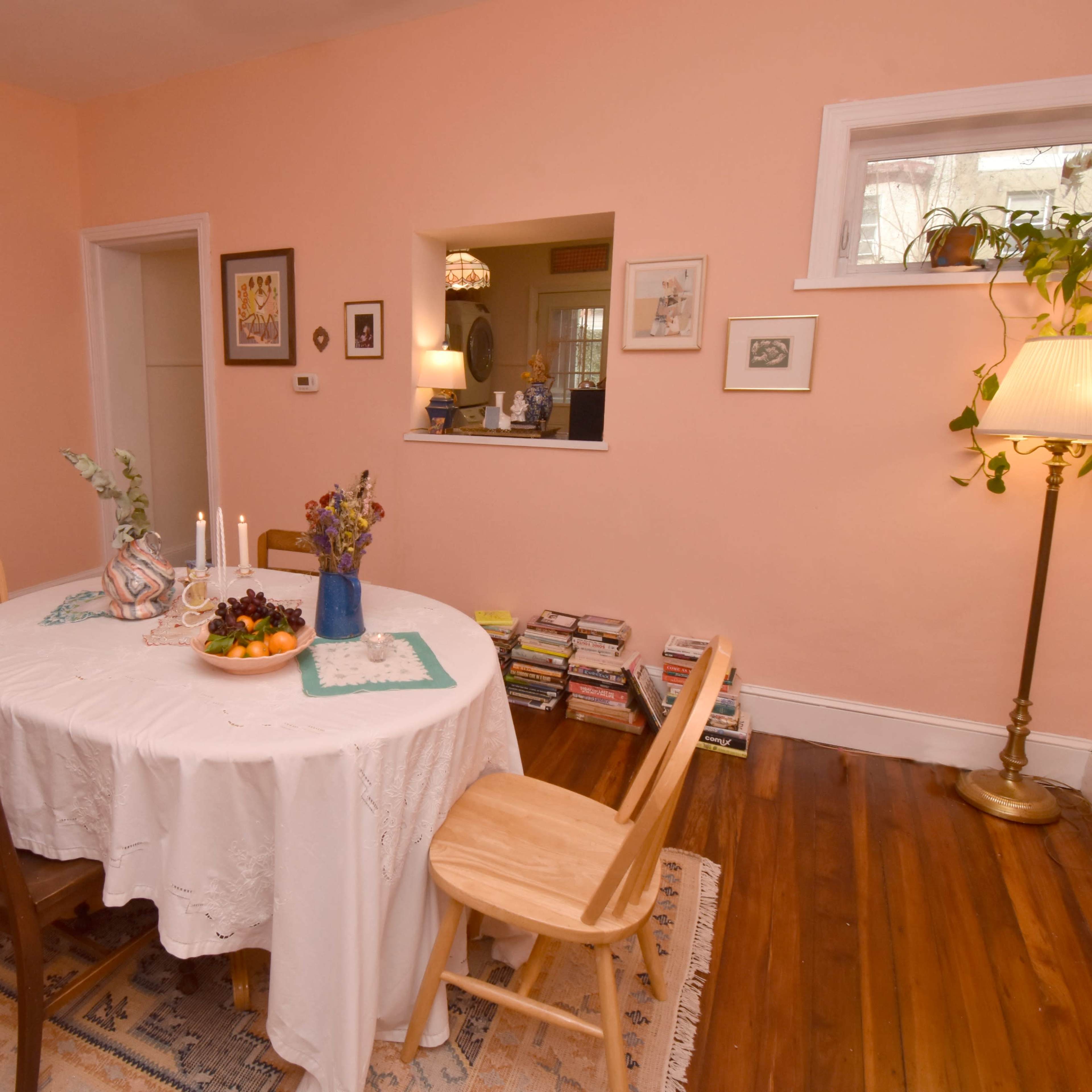 A simple dining area with a round table covered in a white tablecloth, surrounded by wooden chairs, and a warm-colored wall illuminated by a lamp.