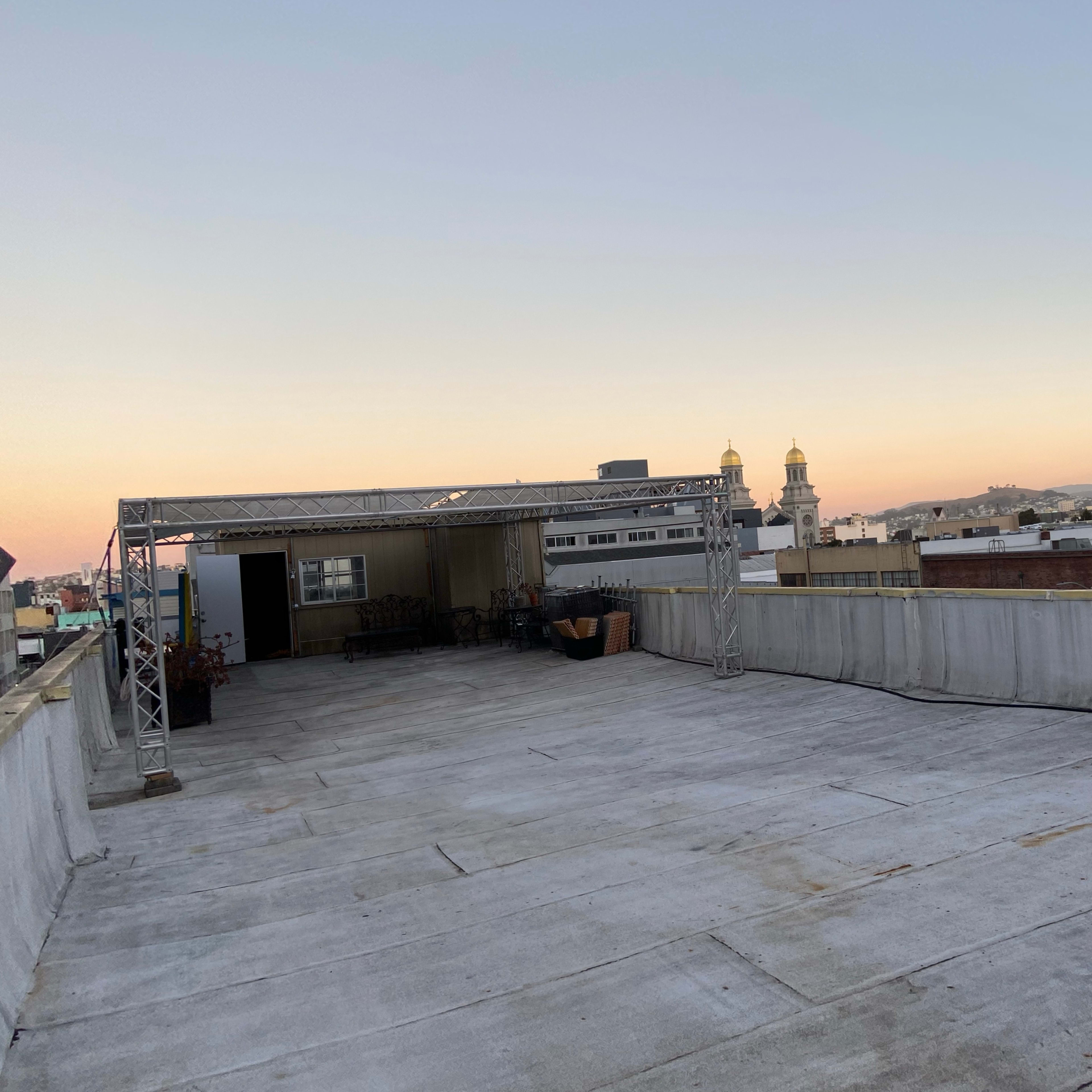 A flat rooftop with a metal structure and a view of buildings and a distant dome at sunset.