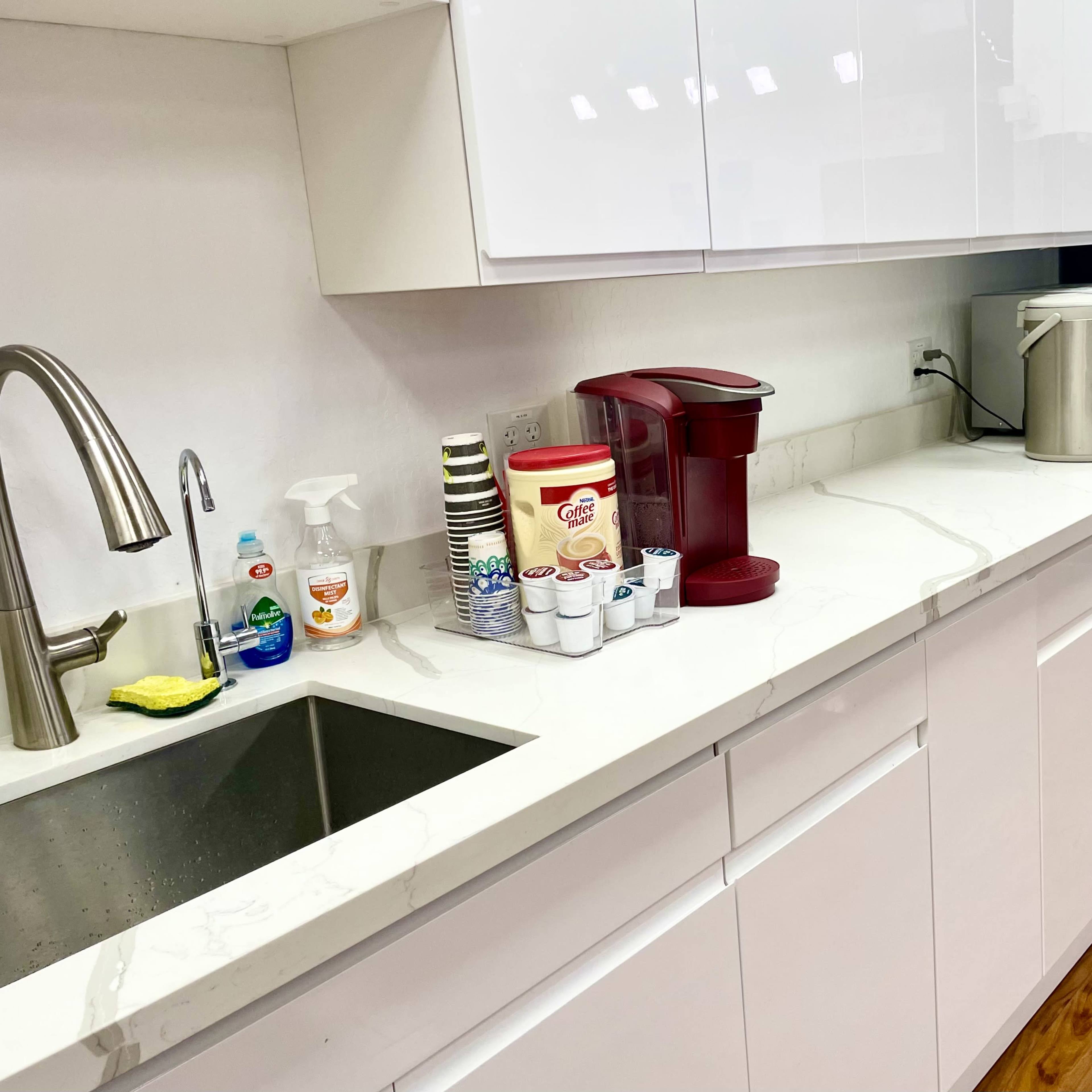 A modern kitchen with a sink, coffee maker, microwave, and a refrigerator along a clean countertop.