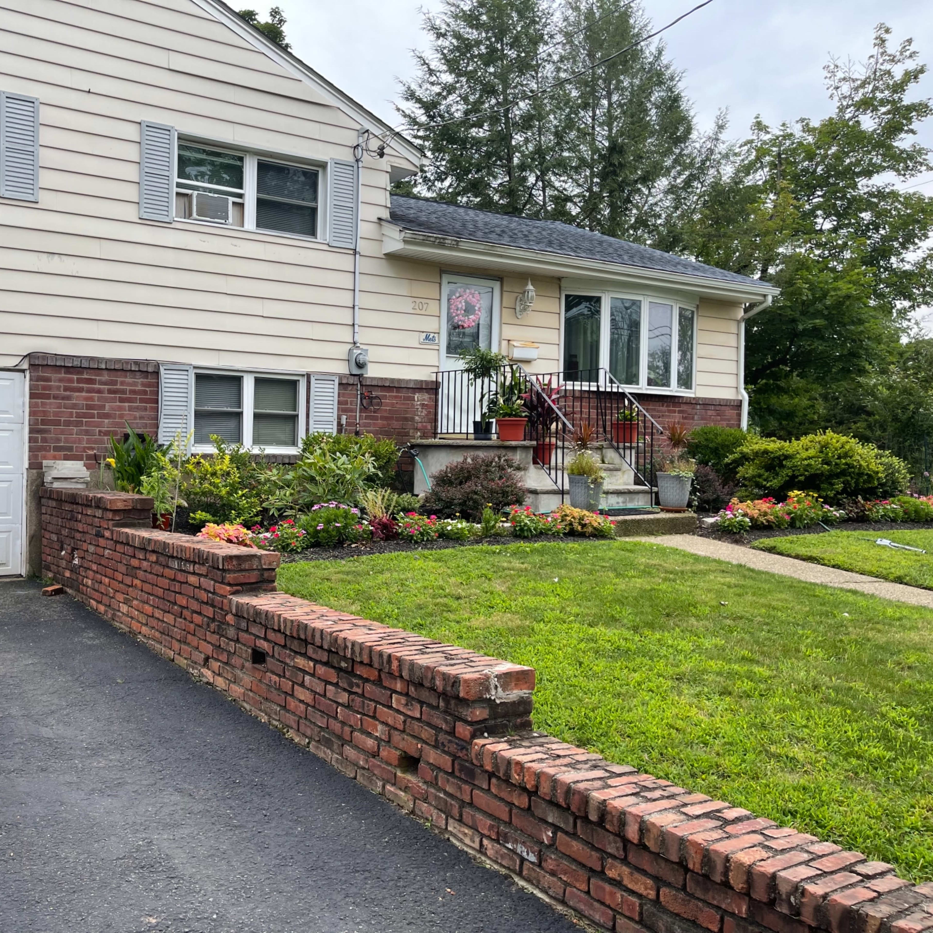 A two-story house with a brick front wall, a garage, and a well-maintained flower garden in the front yard.
