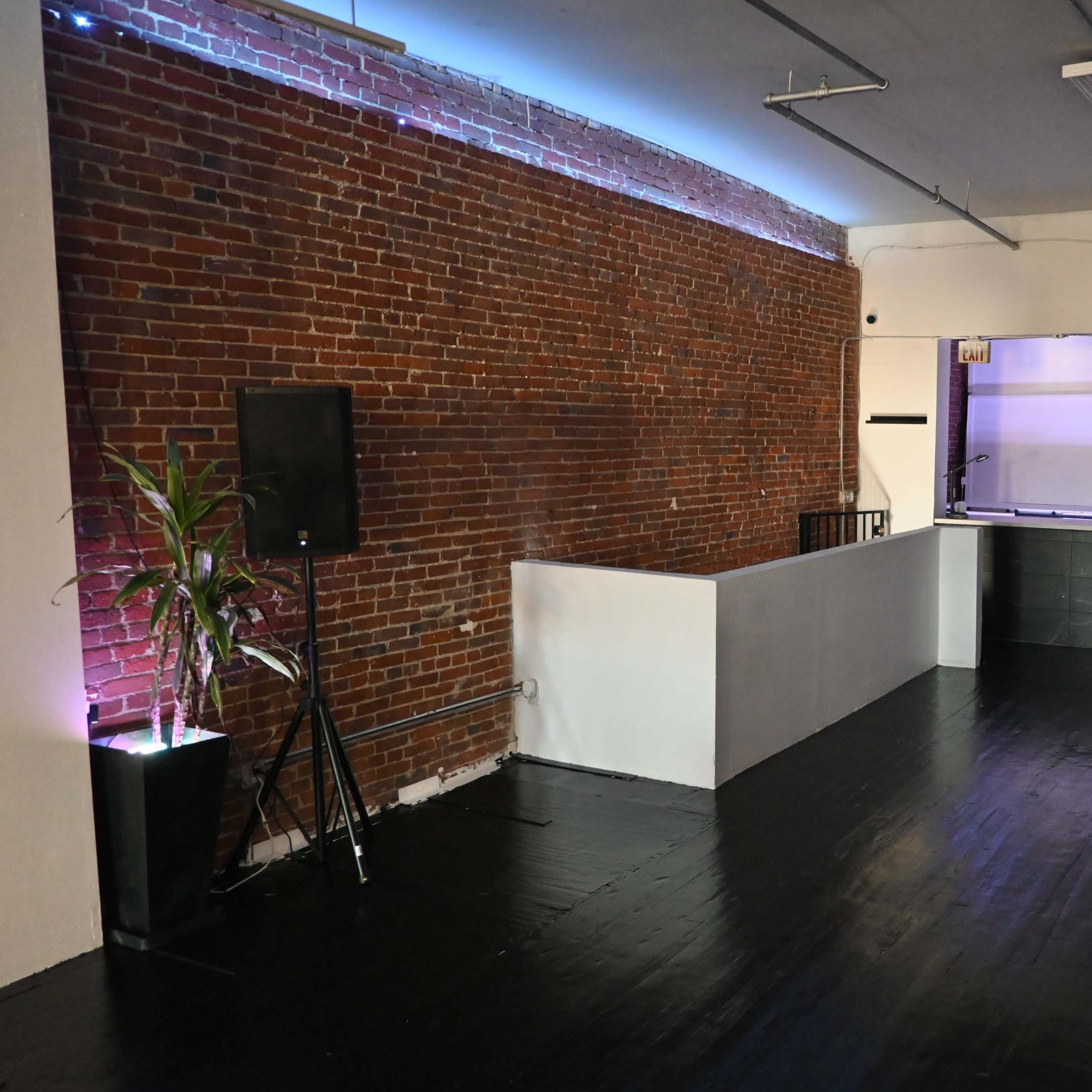 A spacious interior with exposed brick walls, a sleek black floor, and a reception area featuring a low counter and ambient lighting.