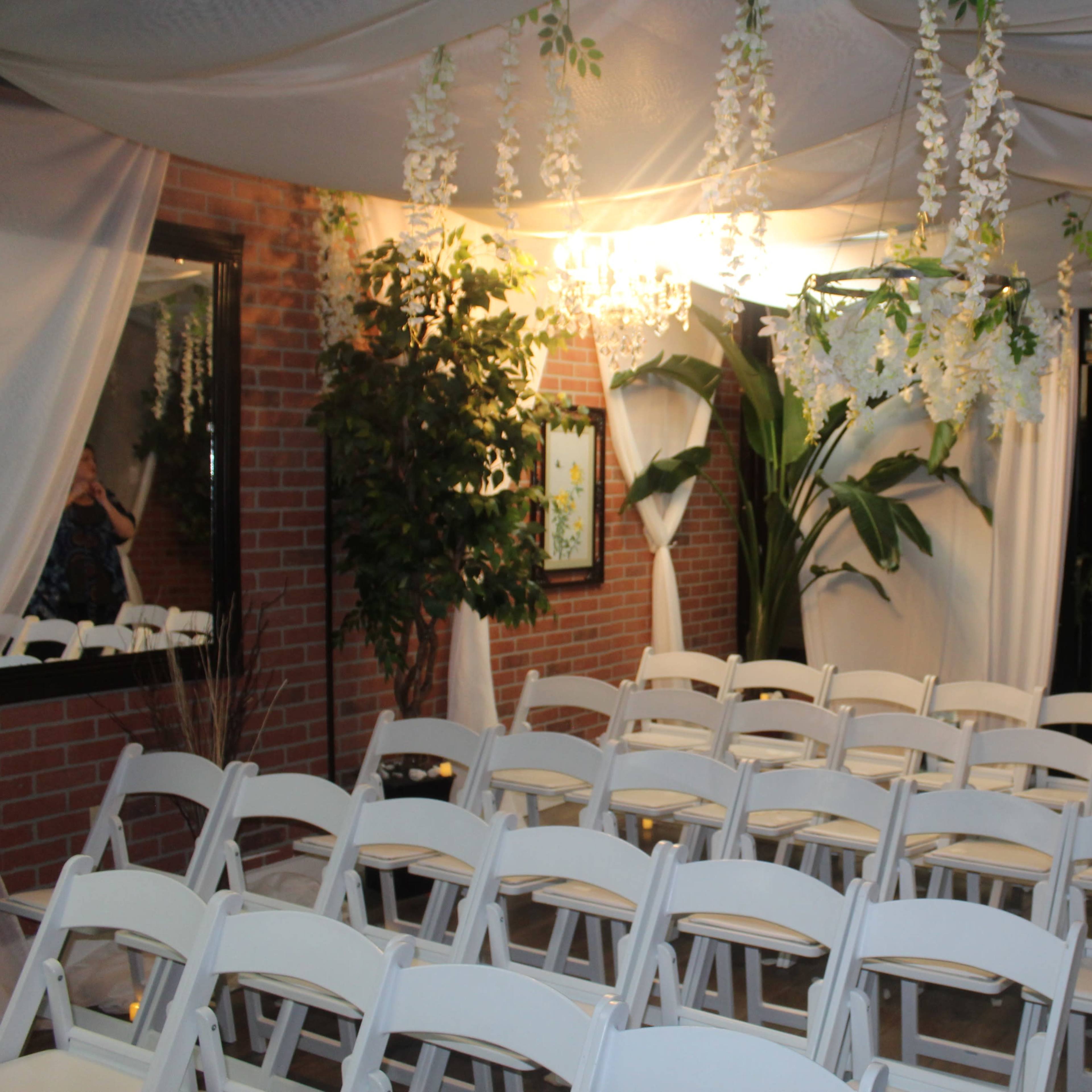 A decorated indoor venue with rows of white chairs arranged facing a large window, adorned with floral decorations and draped fabric.