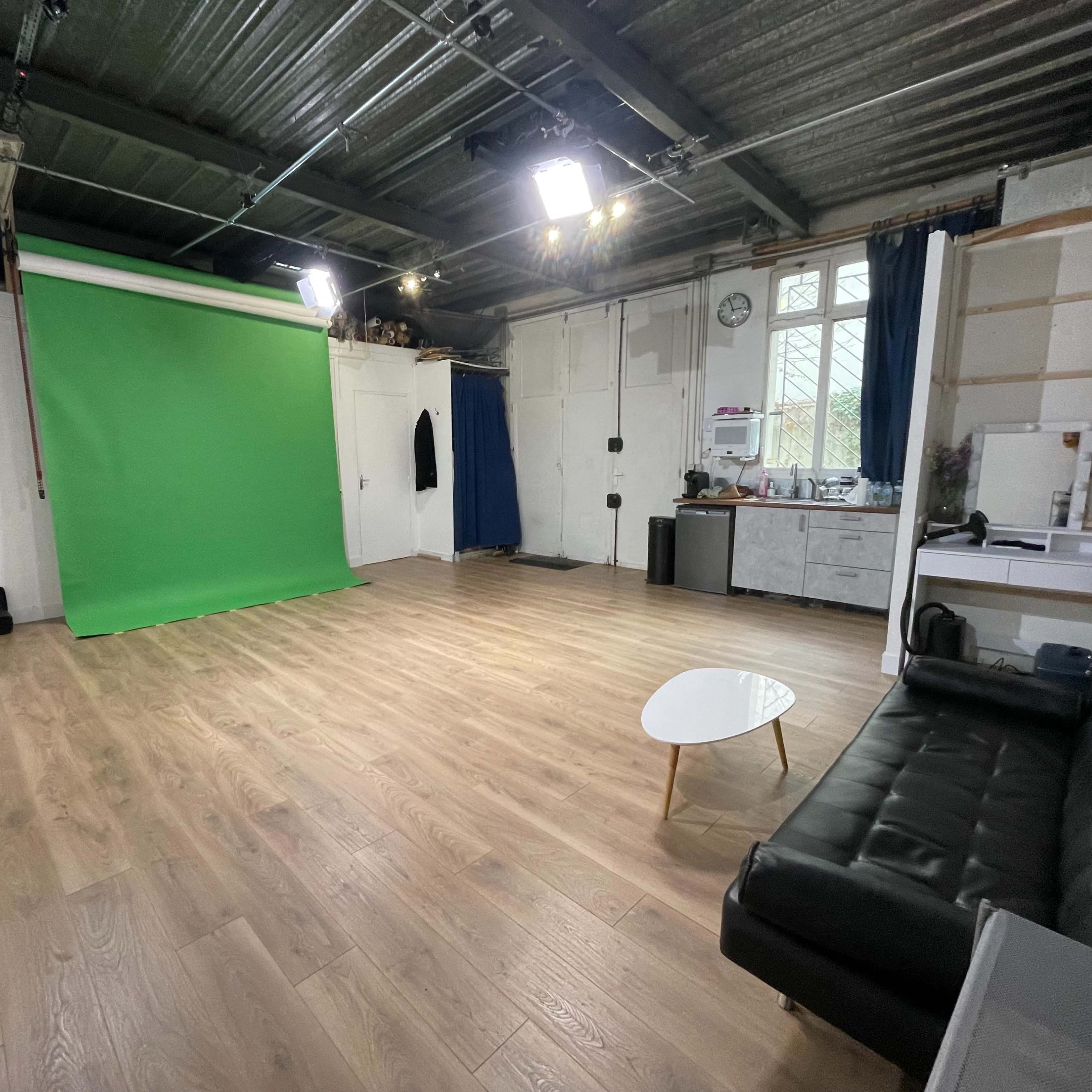 A spacious room with a green backdrop, wooden flooring, and minimal furniture including a black couch and a small table.