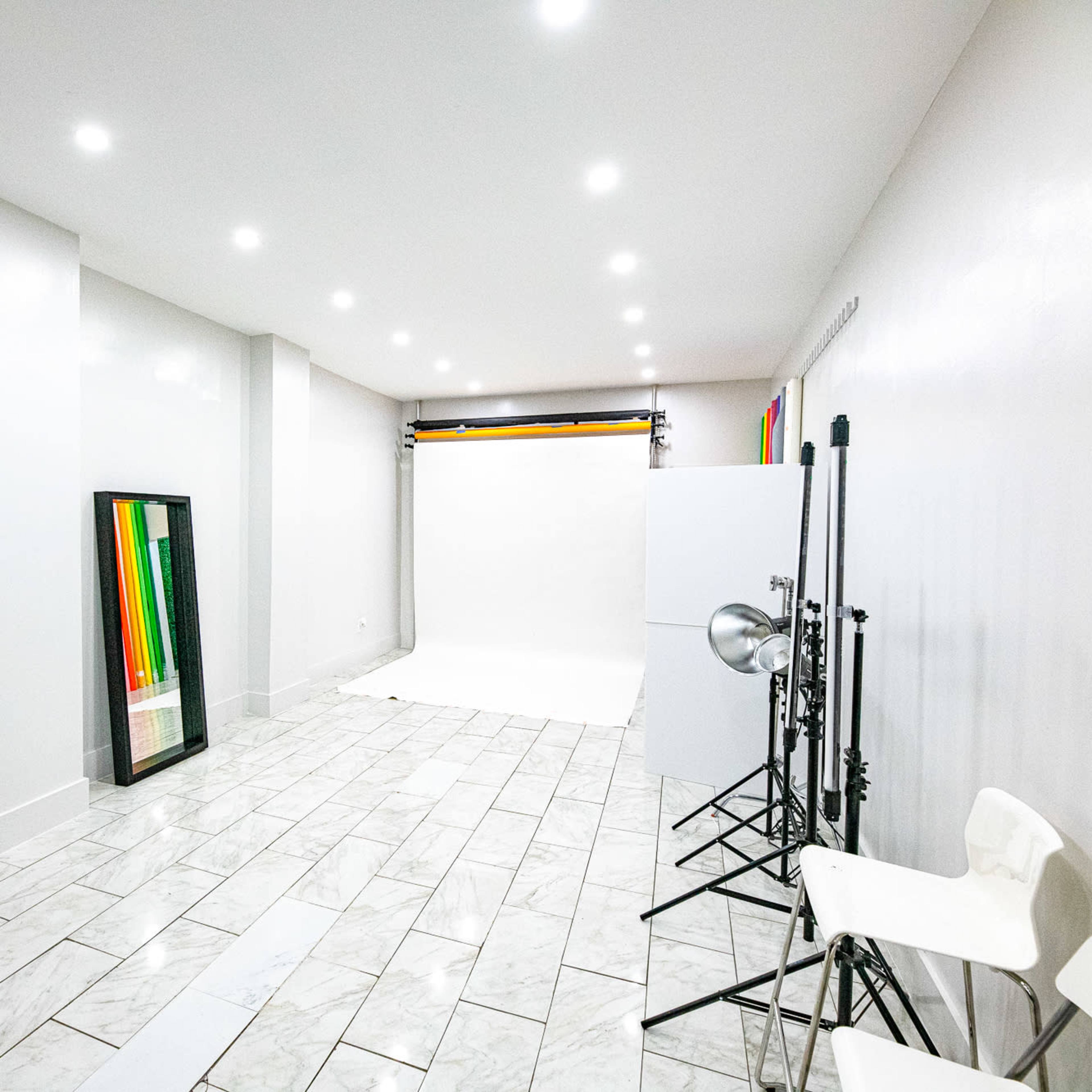 A spacious photography studio with white walls, a seamless backdrop, and various equipment including tripods and lights.