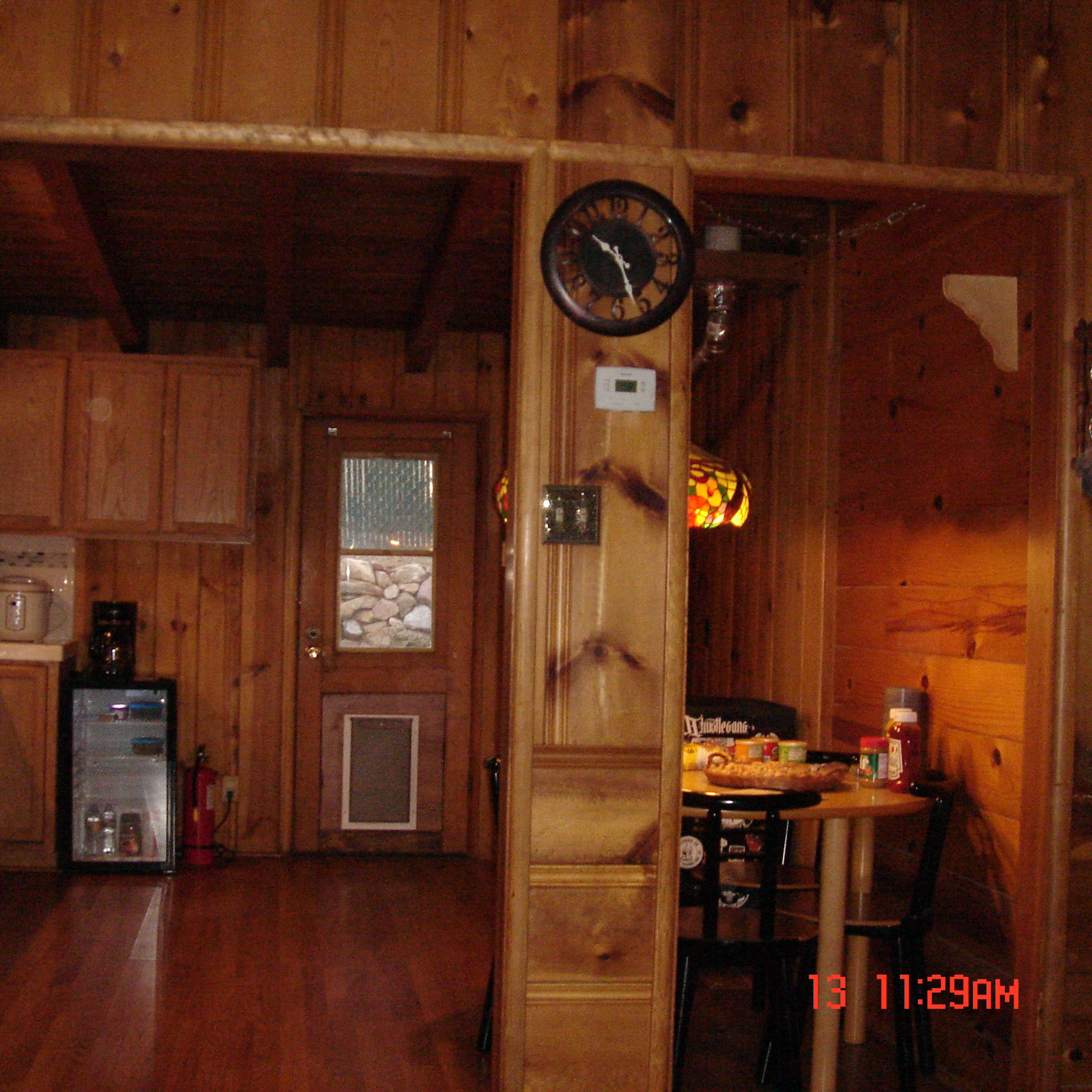 A wooden interior of a small kitchen and dining area with a clock on the wall and a table set for meals.
