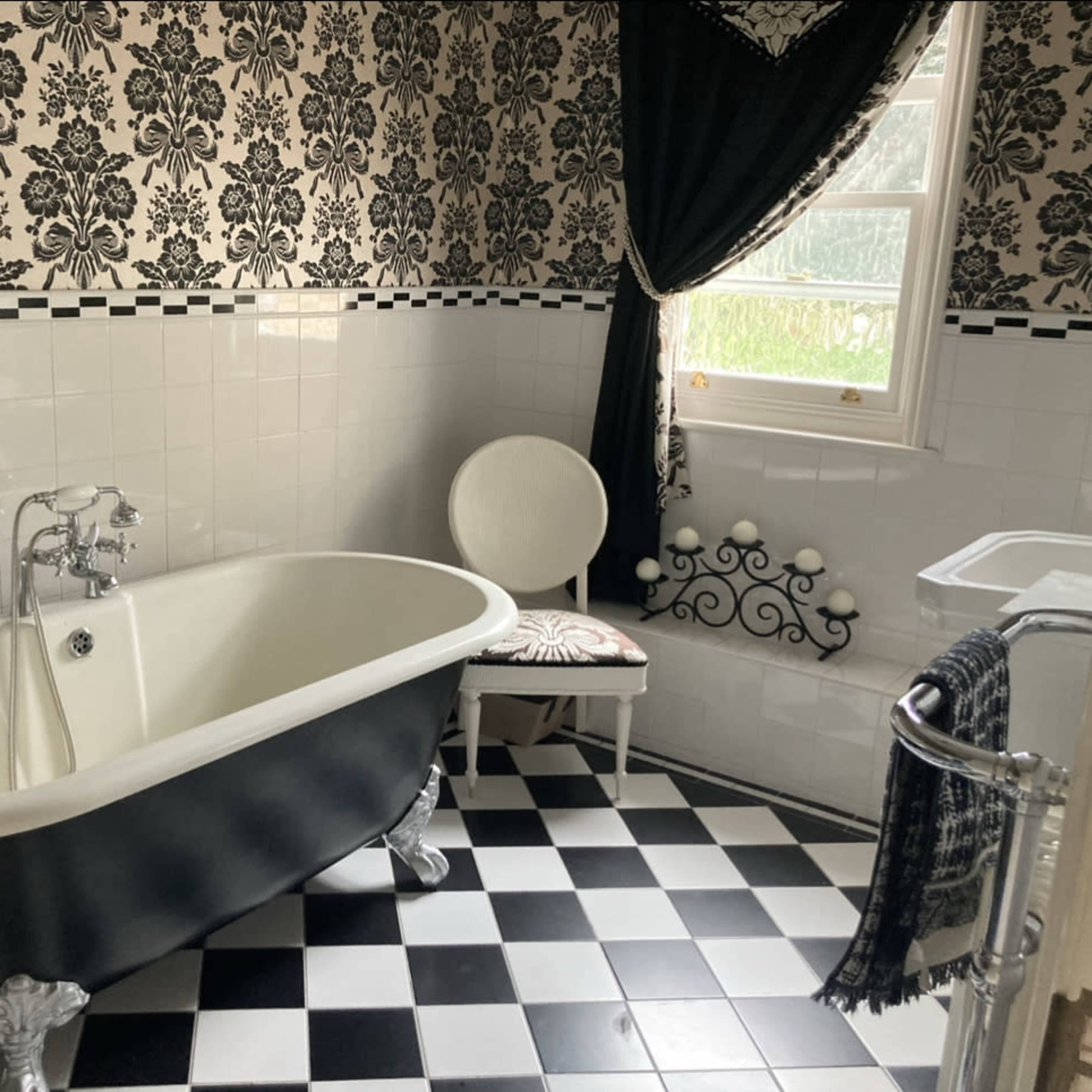 A vintage-style bathroom with a black and white checkerboard floor, a clawfoot bathtub, and patterned wallpaper.
