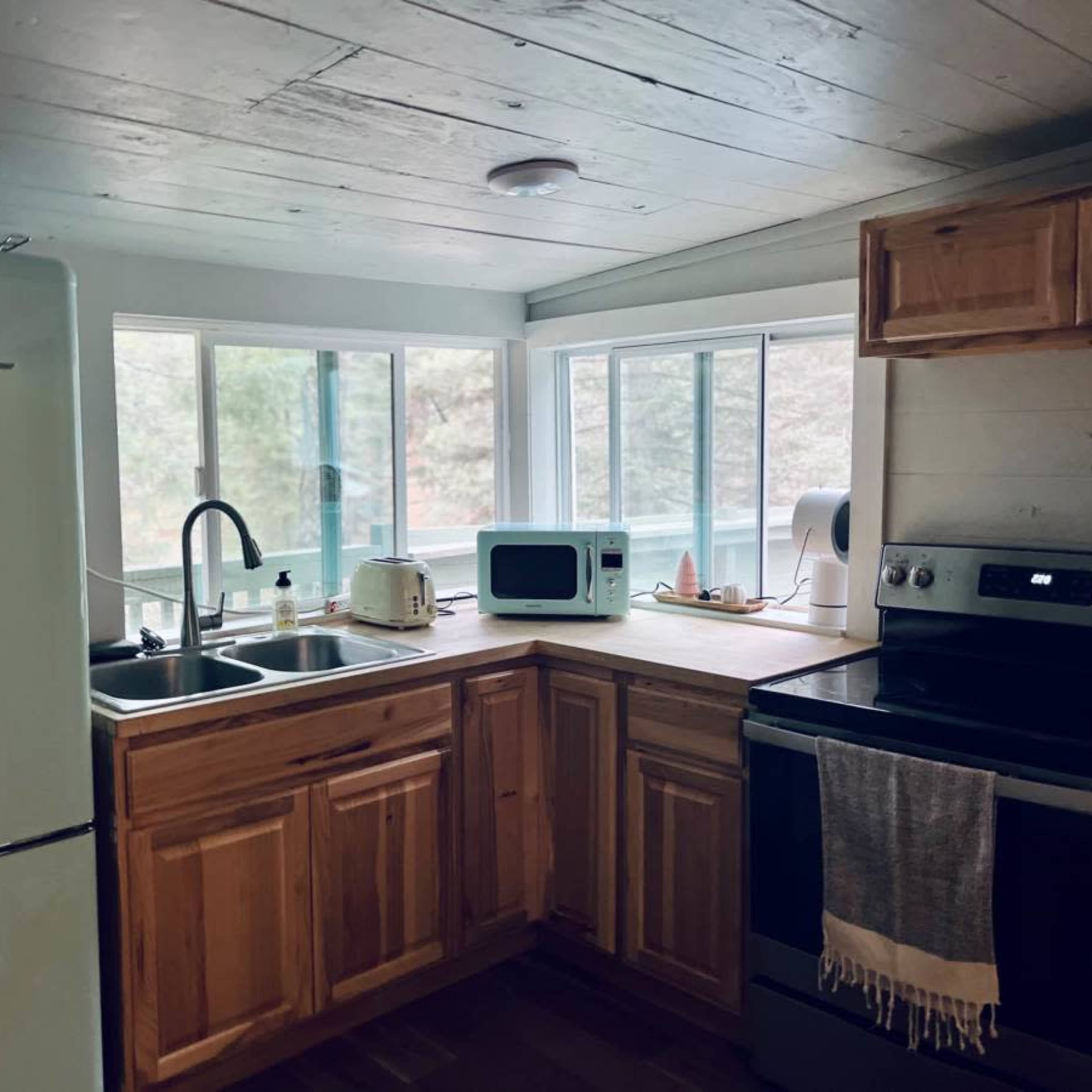 A kitchen with wooden cabinets, a stainless steel stove, a green retro refrigerator, and large windows allowing natural light.