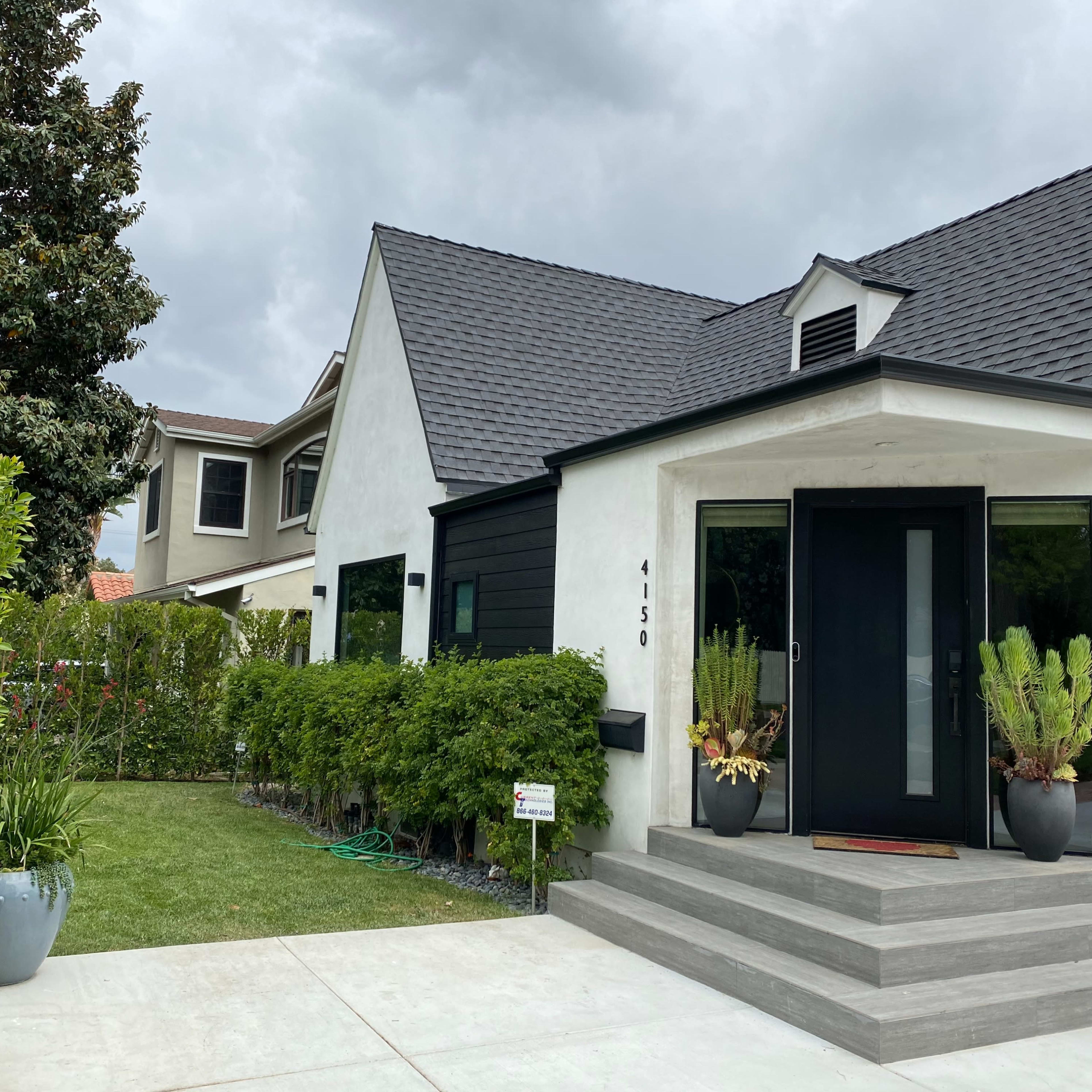 A modern house features a black and white exterior with a small front garden and a concrete walkway leading to the entrance.