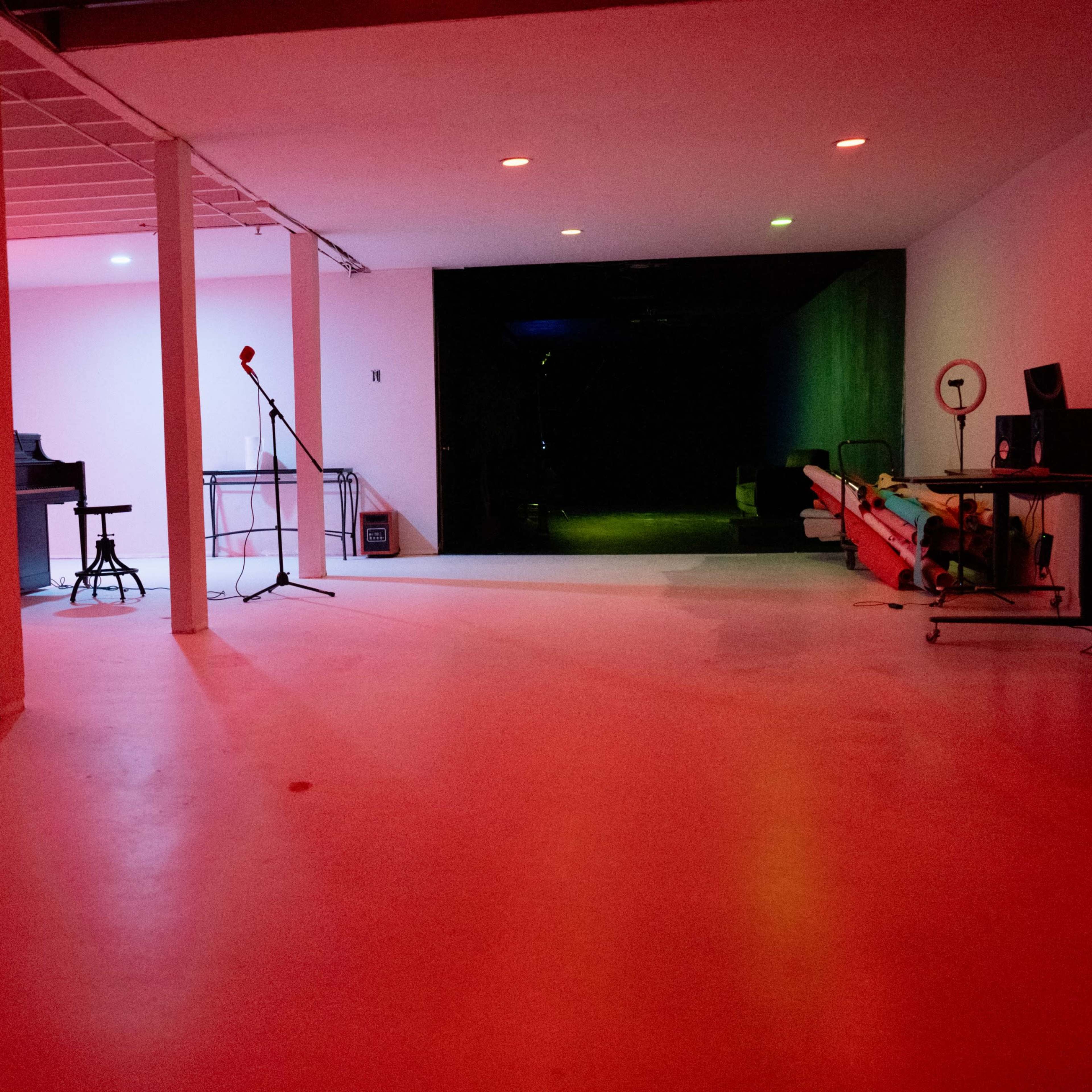 An empty studio space with a mic stand, a bar stool, and various illuminated areas in red and green light.