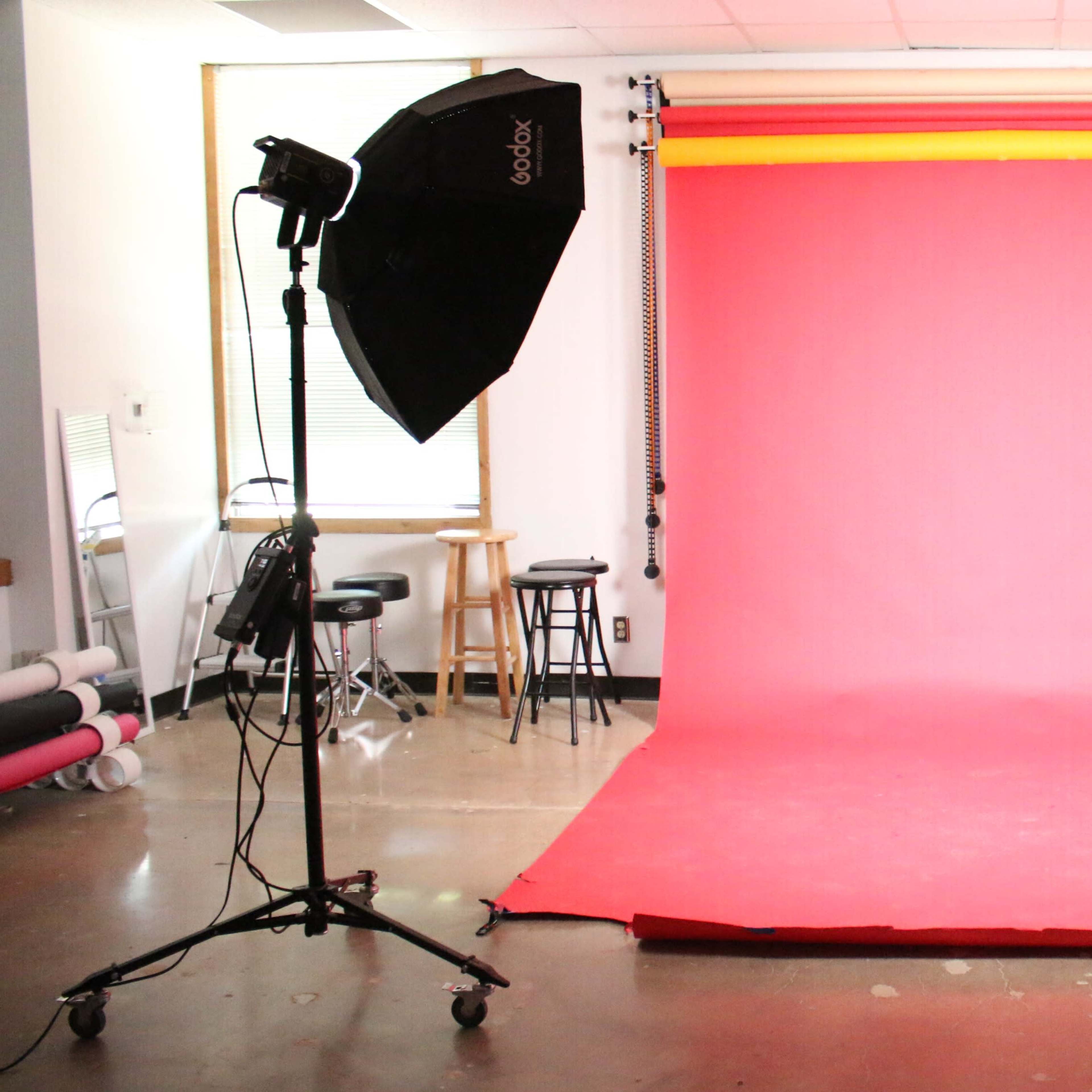 A photography studio setup with a pink backdrop and two softbox lights on either side.