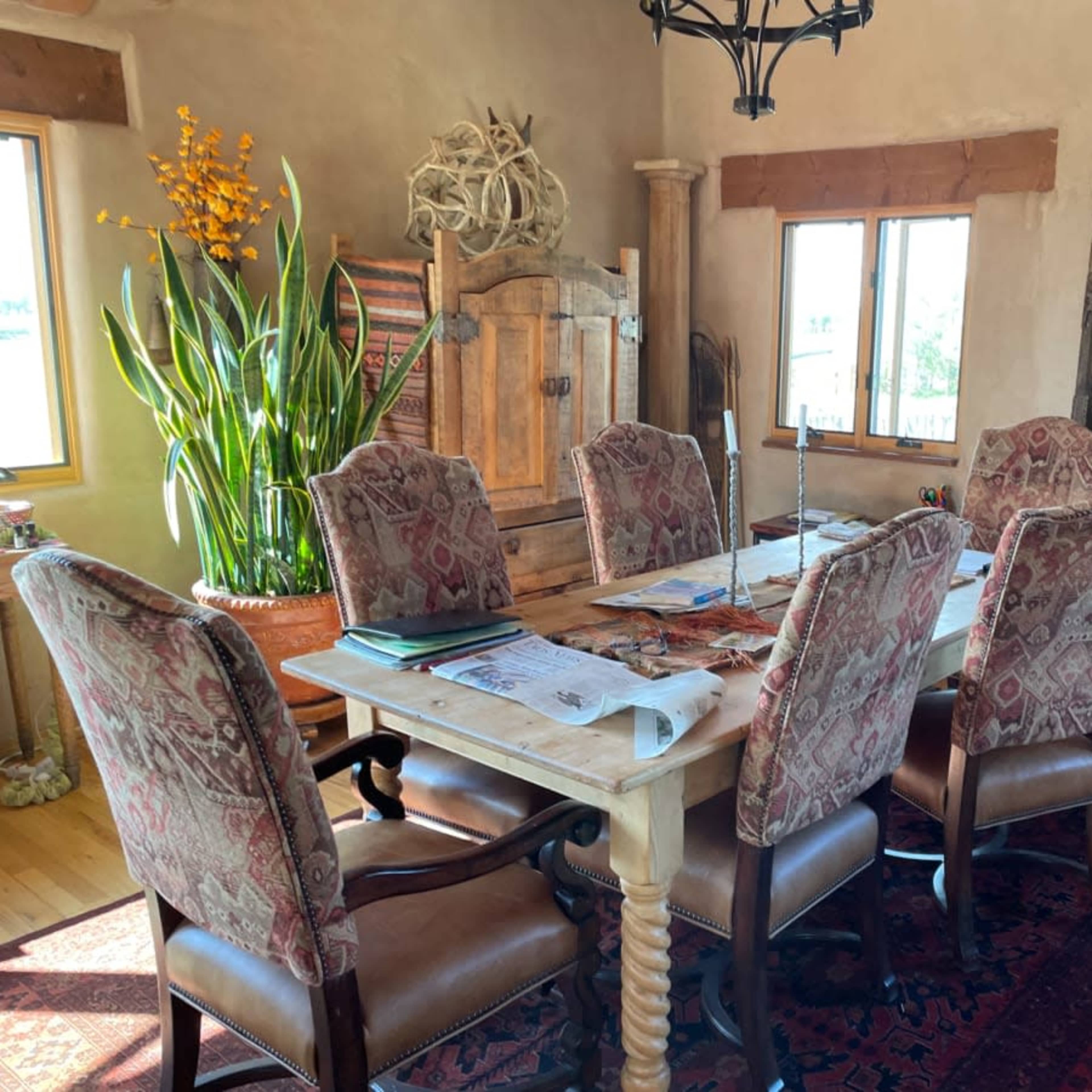 A spacious dining room features a wooden table surrounded by six upholstered chairs, with large windows and a decorative fireplace in the background.