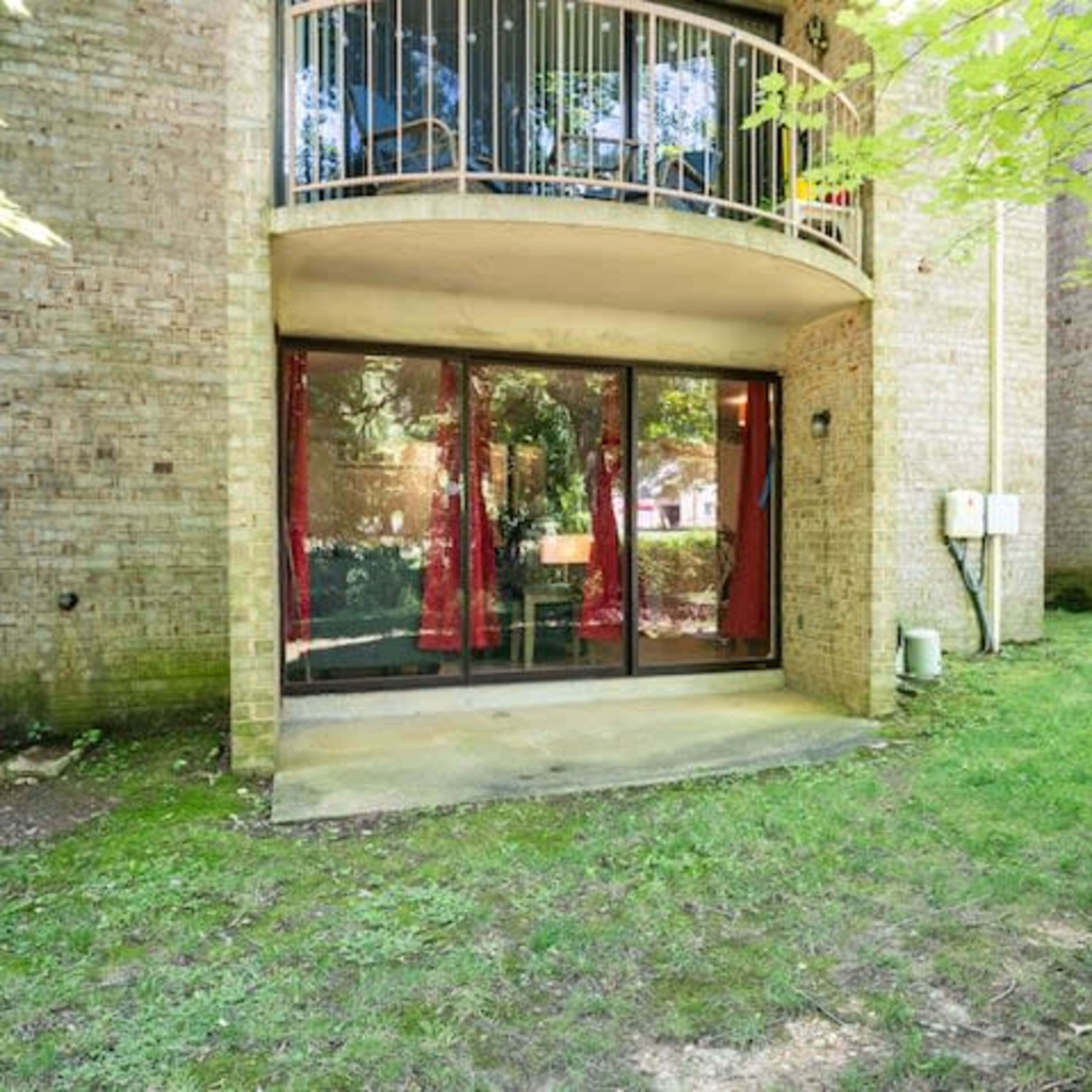 A ground-level patio area with glass doors and a view of a grassy green space surrounded by brick buildings.
