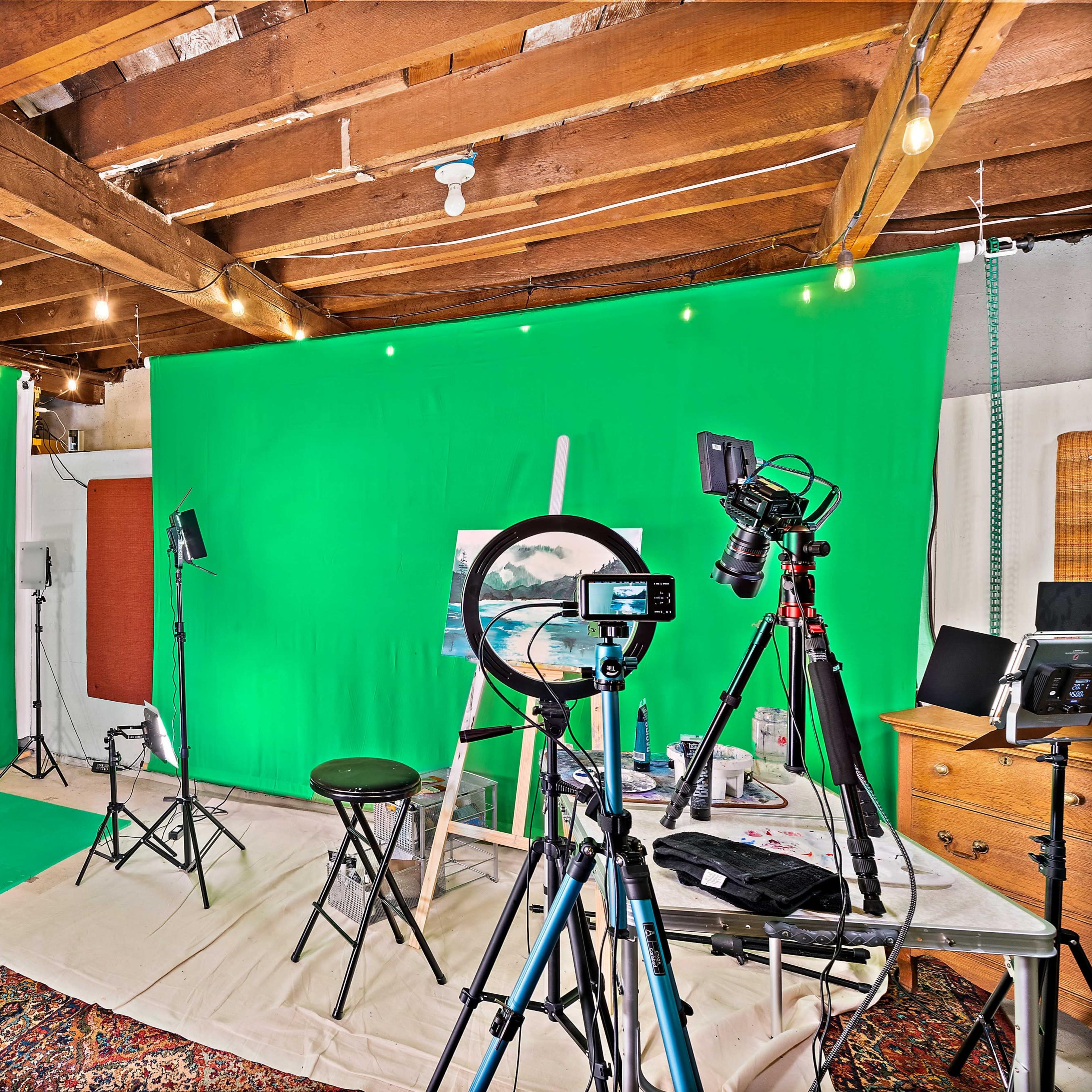 A green studio setup with lighting equipment, cameras on tripods, and a workspace for painting.