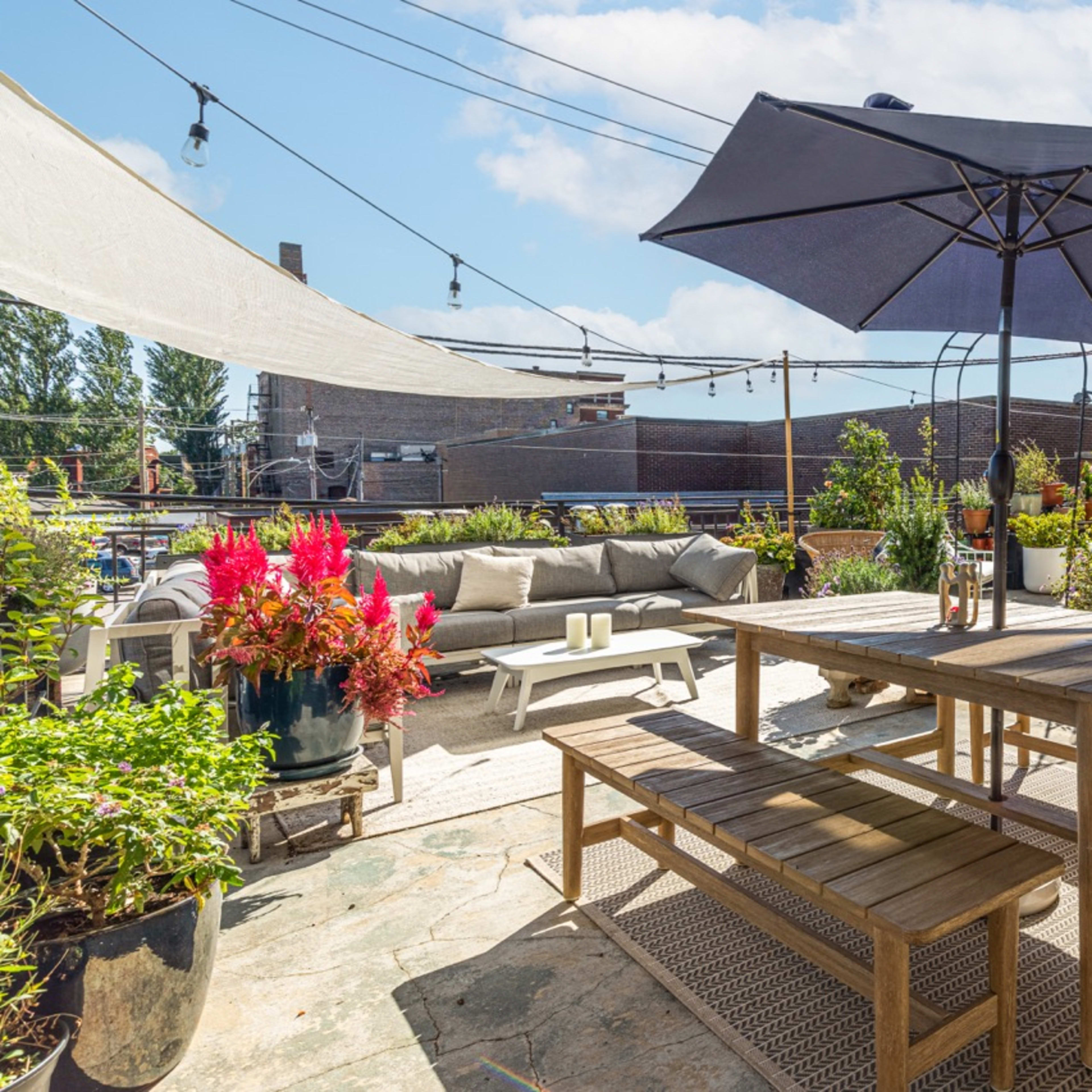 A rooftop patio adorned with a wooden dining table, an umbrella, potted plants, and seating arranged for relaxation.