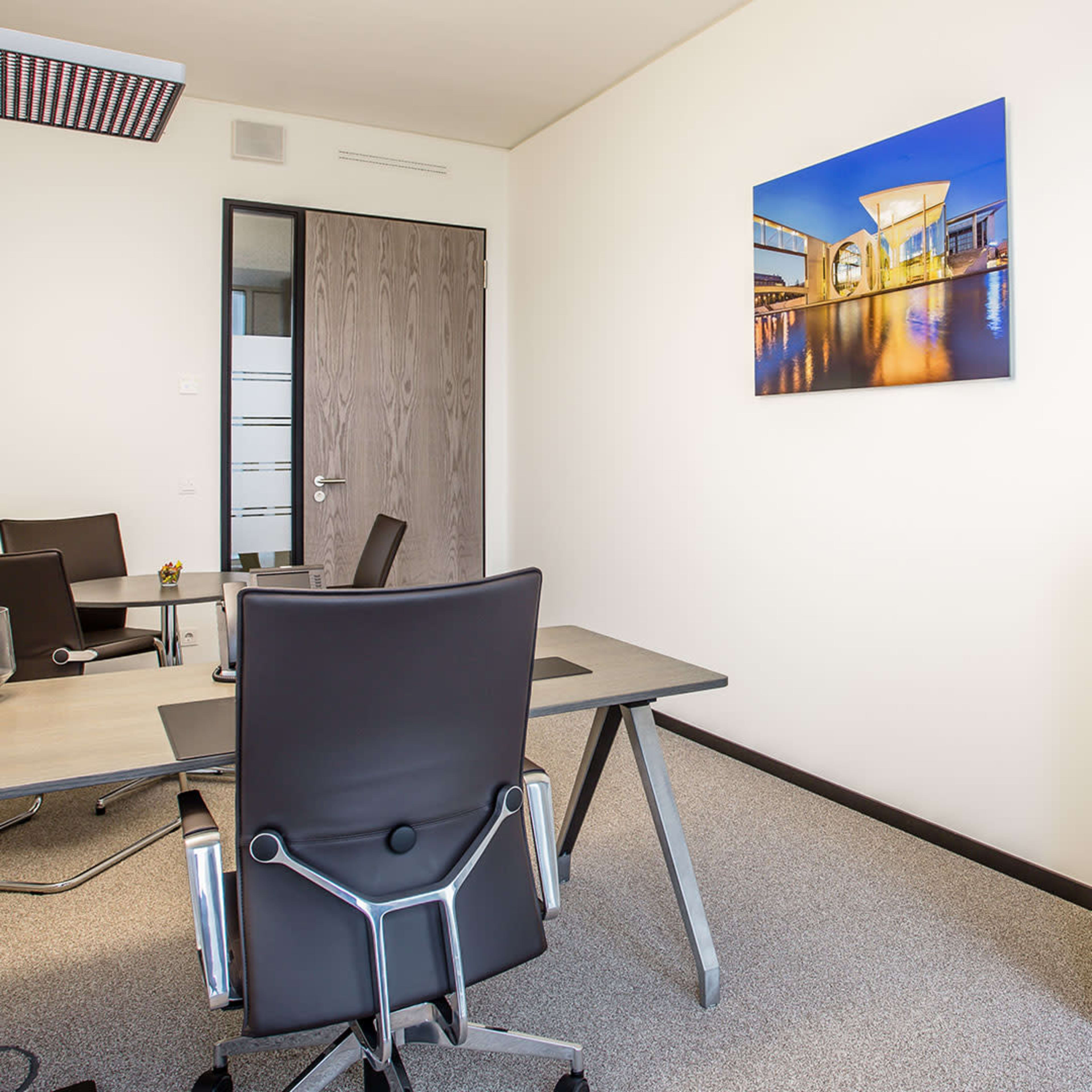 A modern office space featuring a desk, two chairs, a cabinet, and a large wall-mounted photograph.