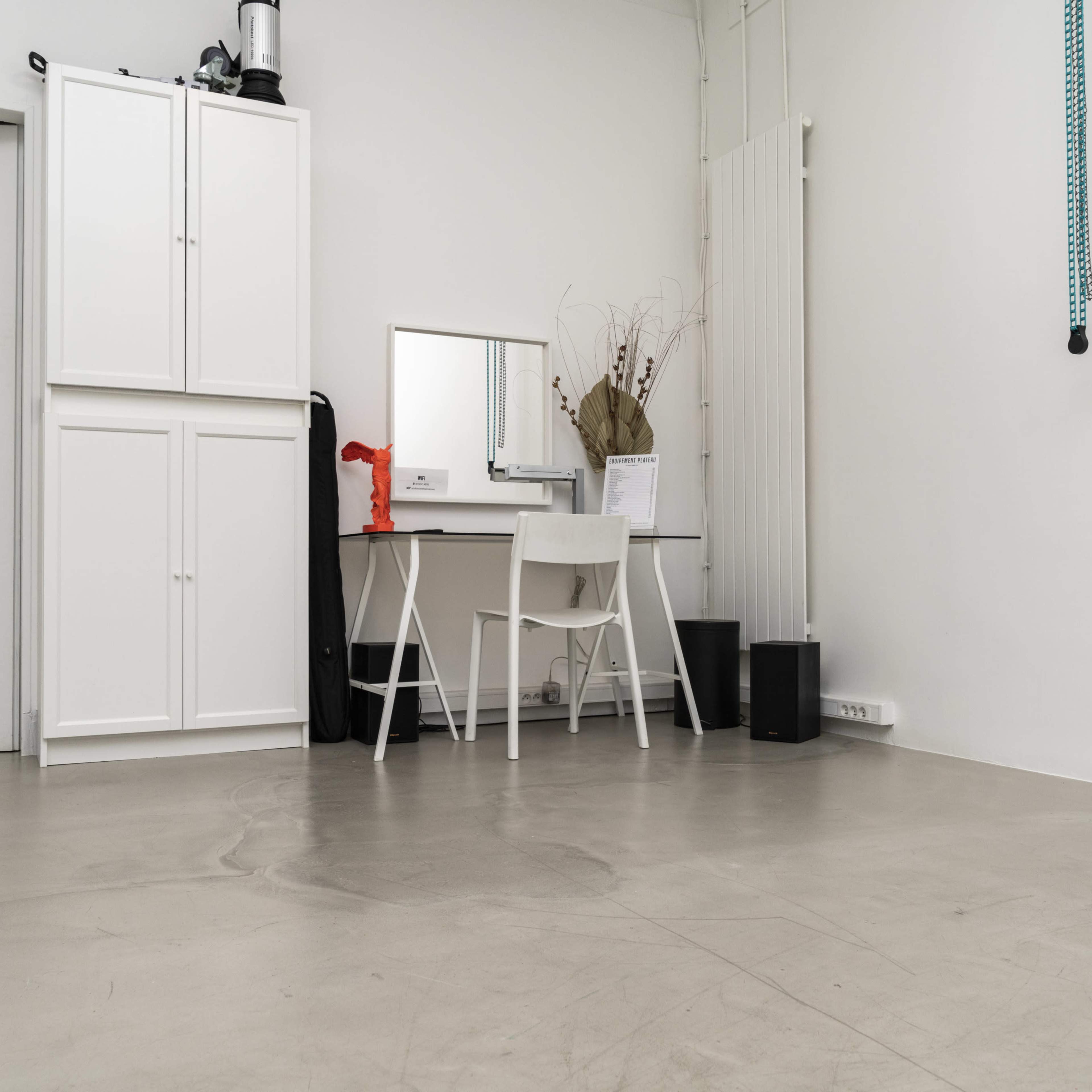 A minimalist interior space featuring a white desk and chair, a mirror, and storage cabinets against a light-colored wall.